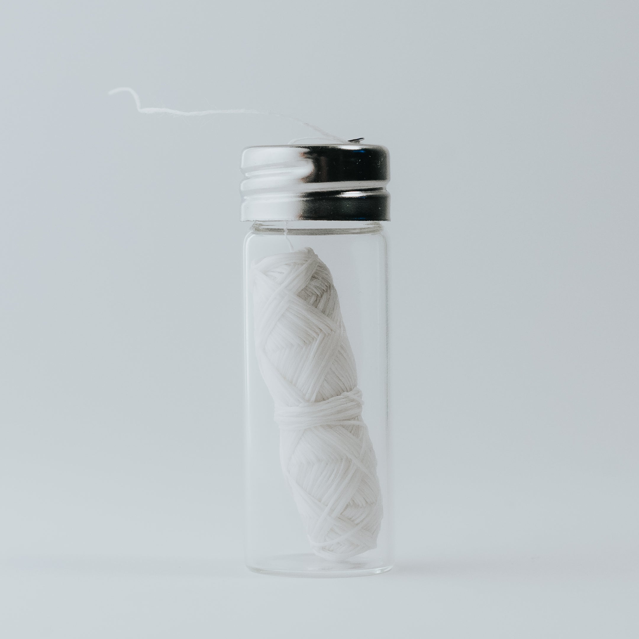 Natural Silk Dental Floss in a reusable glass dispenser with a metal cap, featuring a strong silk thread coated in Candelilla wax and peppermint flavor.