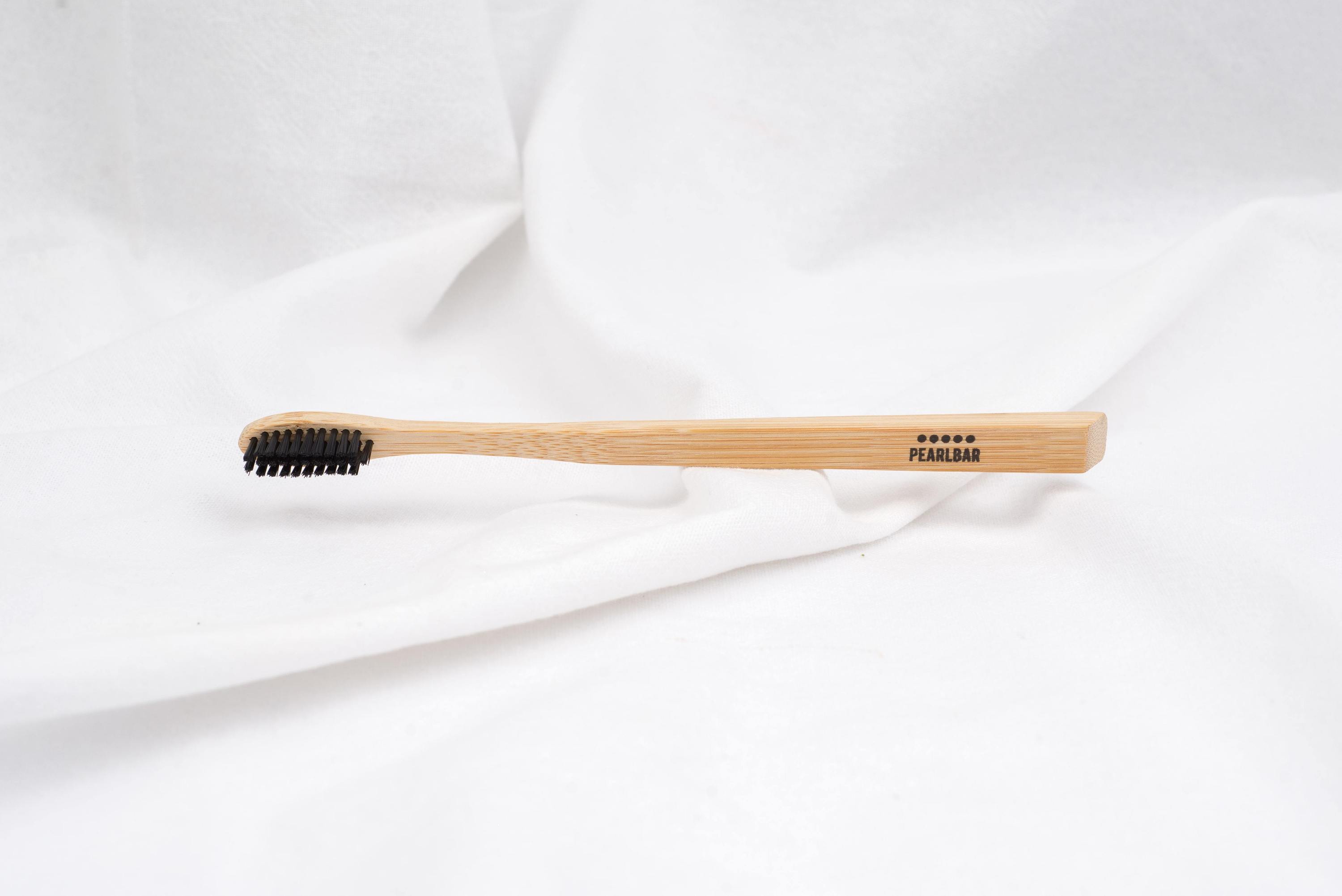 PearlBar Bamboo & Charcoal Toothbrush with a bamboo handle and charcoal-infused bristles, showcasing its eco-friendly design.