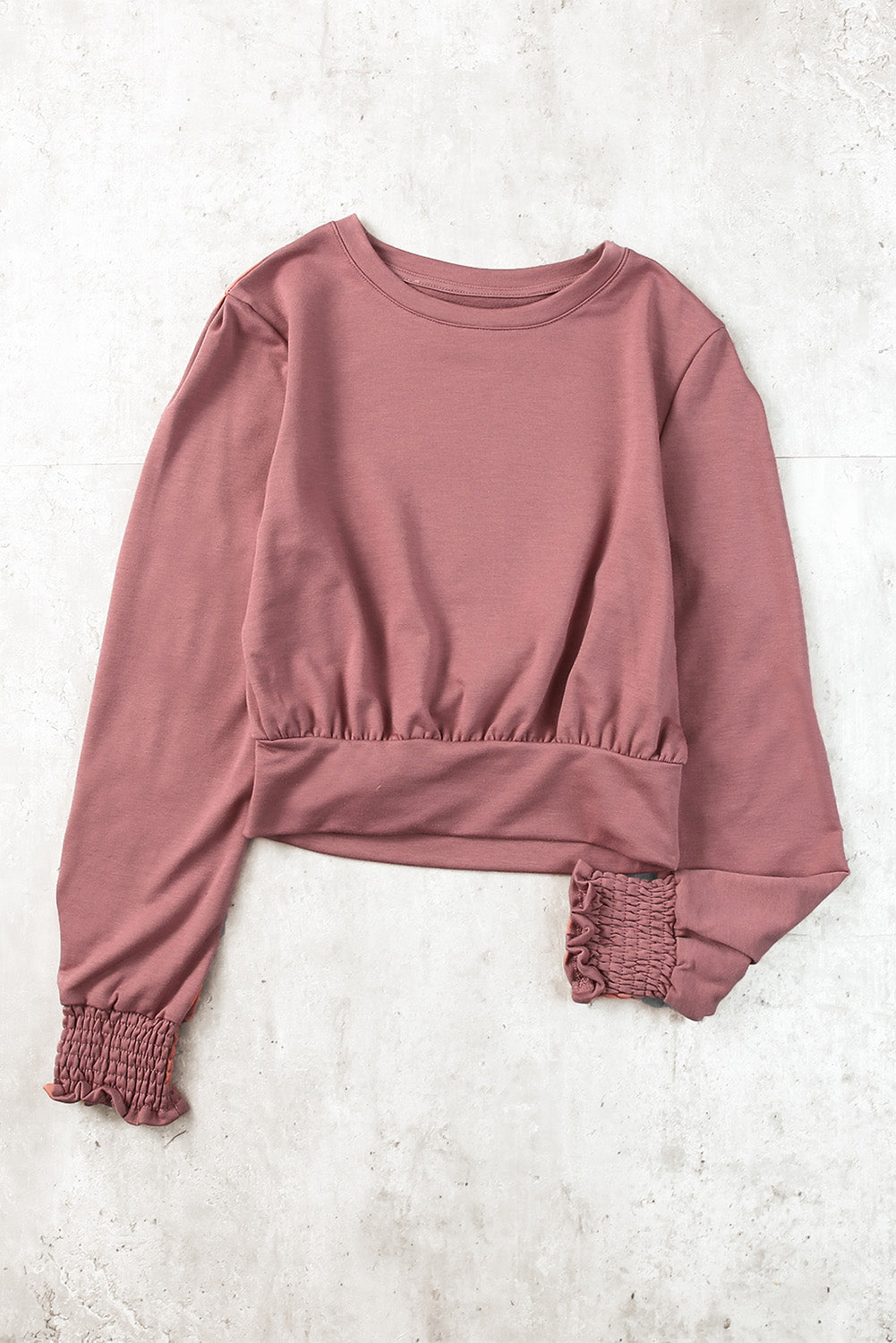 A stylish pink long sleeve crop top with banded hem and smocking cuffs, perfect for casual wear.