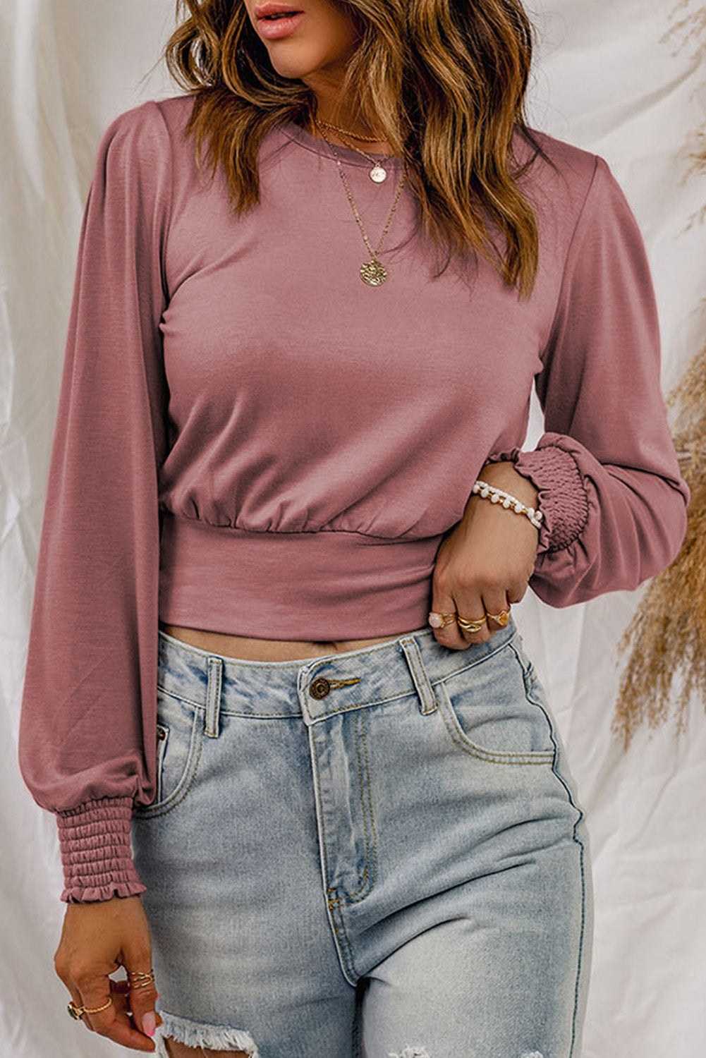 A stylish pink long sleeve crop top with banded hem and smocking cuffs, perfect for casual wear.