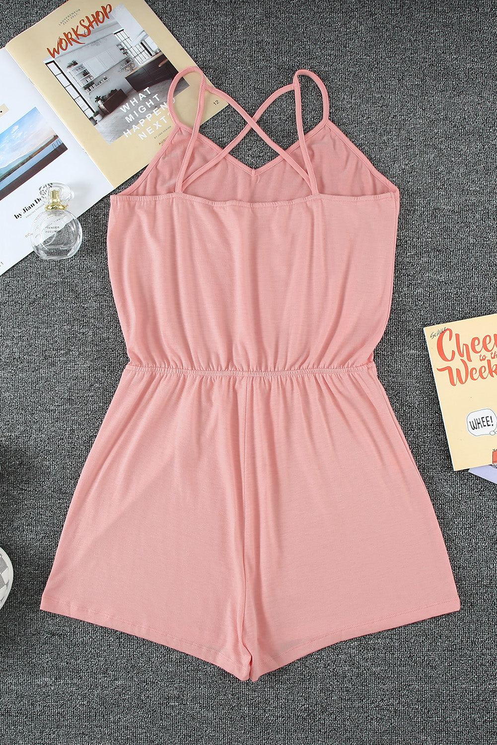 A stylish pink romper featuring spaghetti straps, a V-neckline, and a crisscross back design, perfect for a night out.