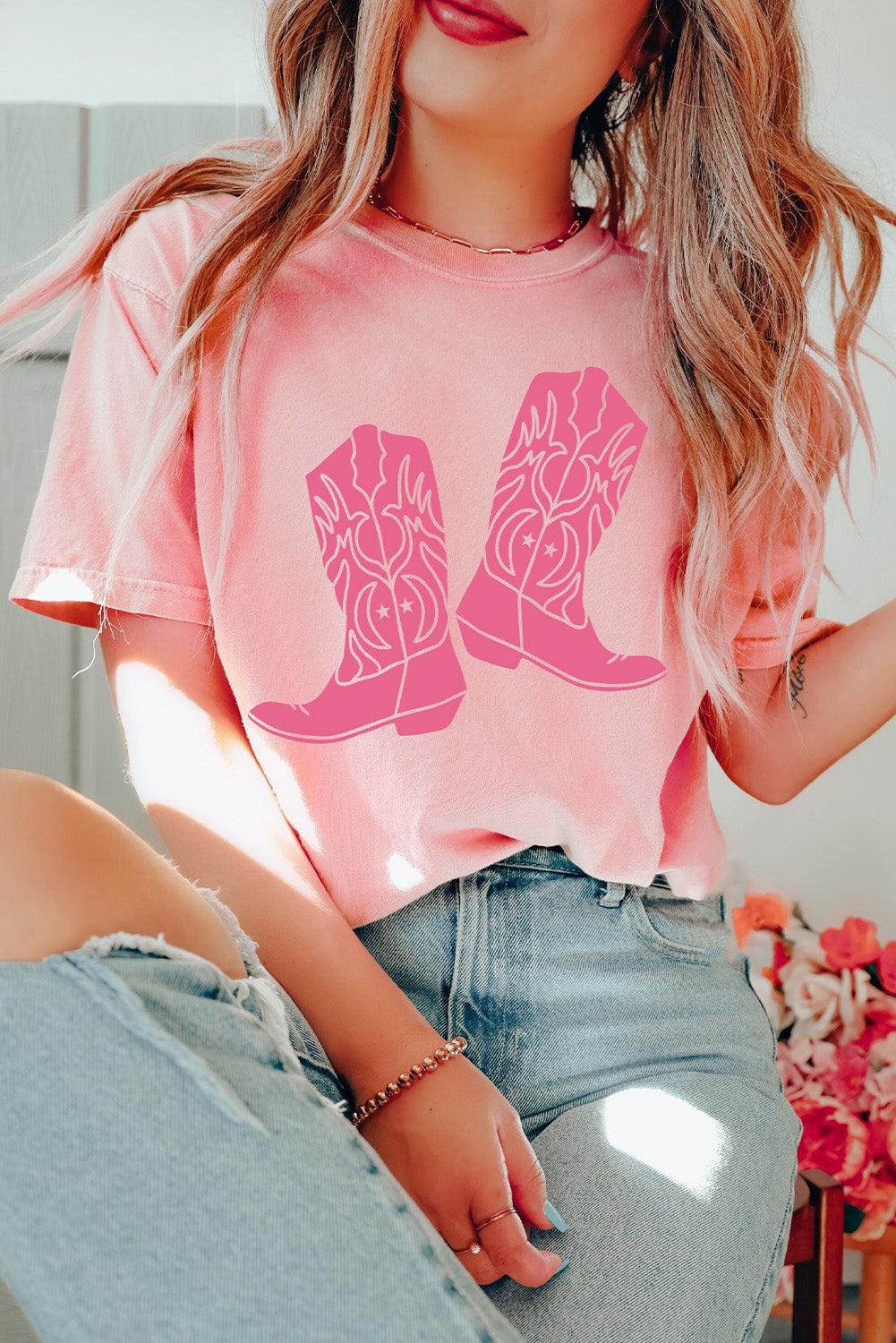 A stylish pink t-shirt featuring a cowboy boots print, perfect for casual wear, with a round neck and short sleeves.