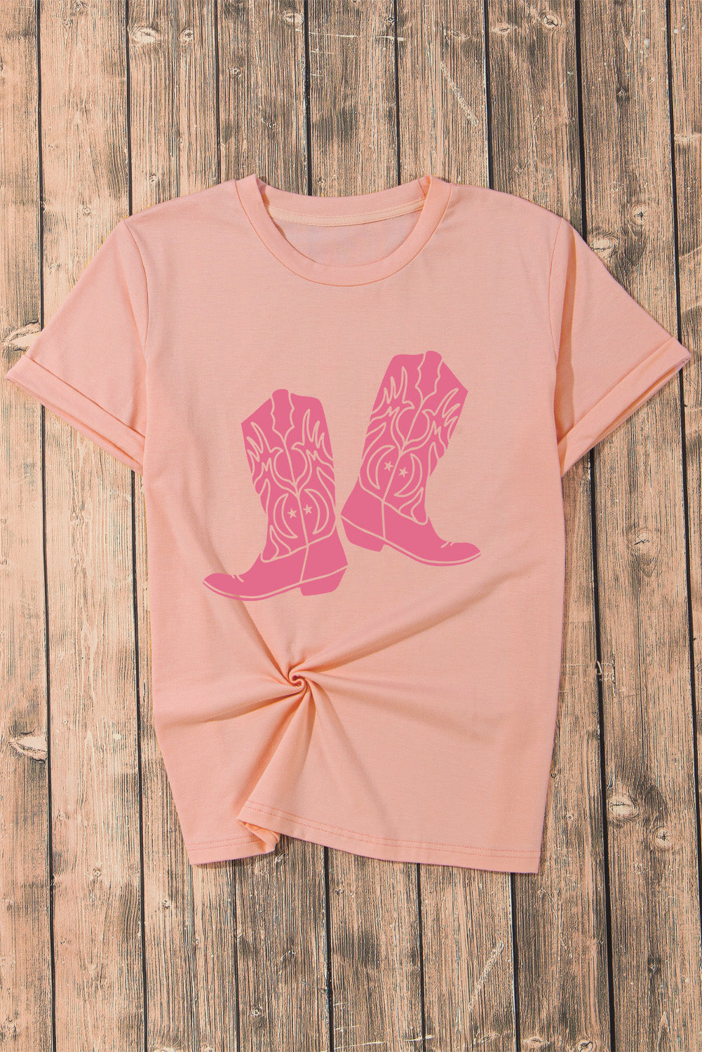 A stylish pink t-shirt featuring a cowboy boots print, perfect for casual wear, with a round neck and short sleeves.