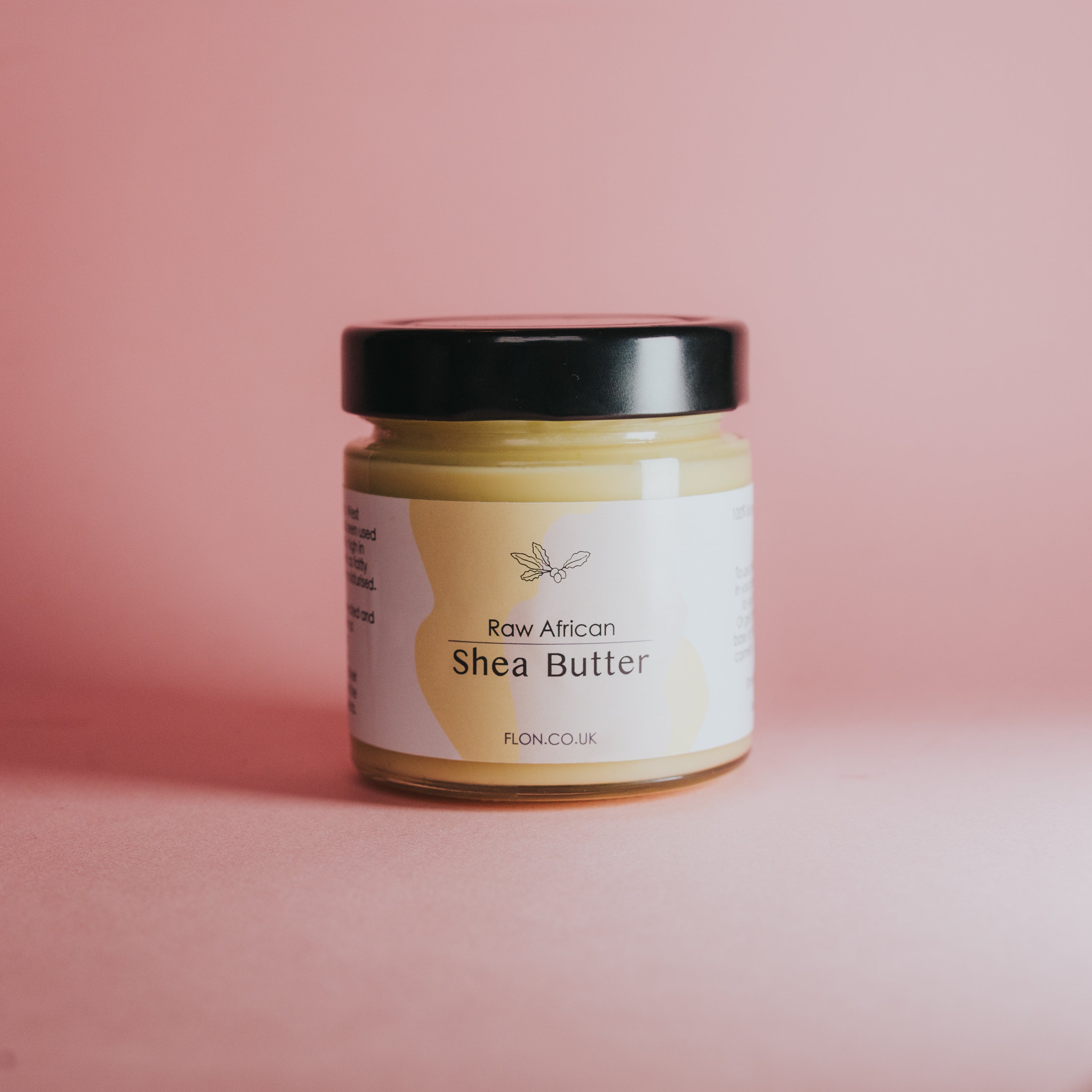 A jar of Raw Unrefined African Shea Butter, showcasing its creamy texture and natural color, surrounded by Shea nuts and leaves.