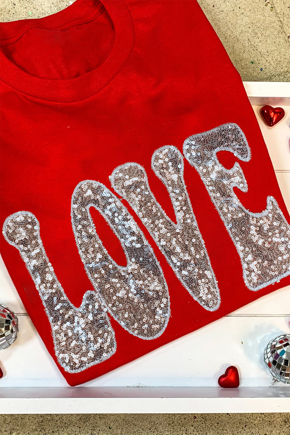 A vibrant red T-shirt featuring a sequined 'LOVE' design, perfect for Valentine's Day and summer wear.