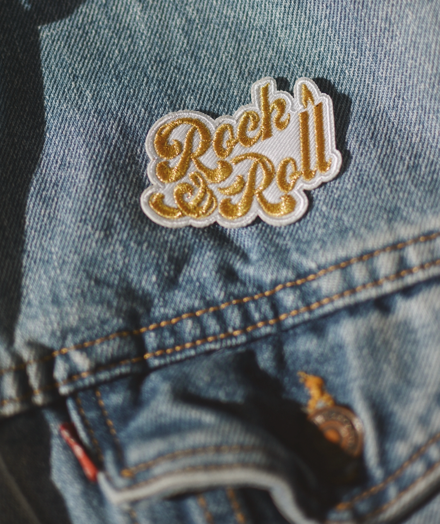 A vibrant 'Rock & Roll' iron-on patch featuring metallic gold thread on a black background, measuring 2.5 inches.