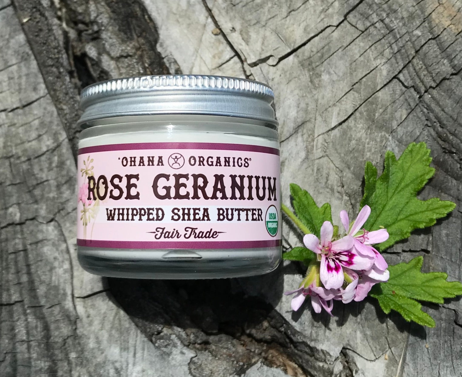 A 2oz recyclable glass jar of Rose Geranium Whipped Shea Butter with a creamy texture, surrounded by rose petals.