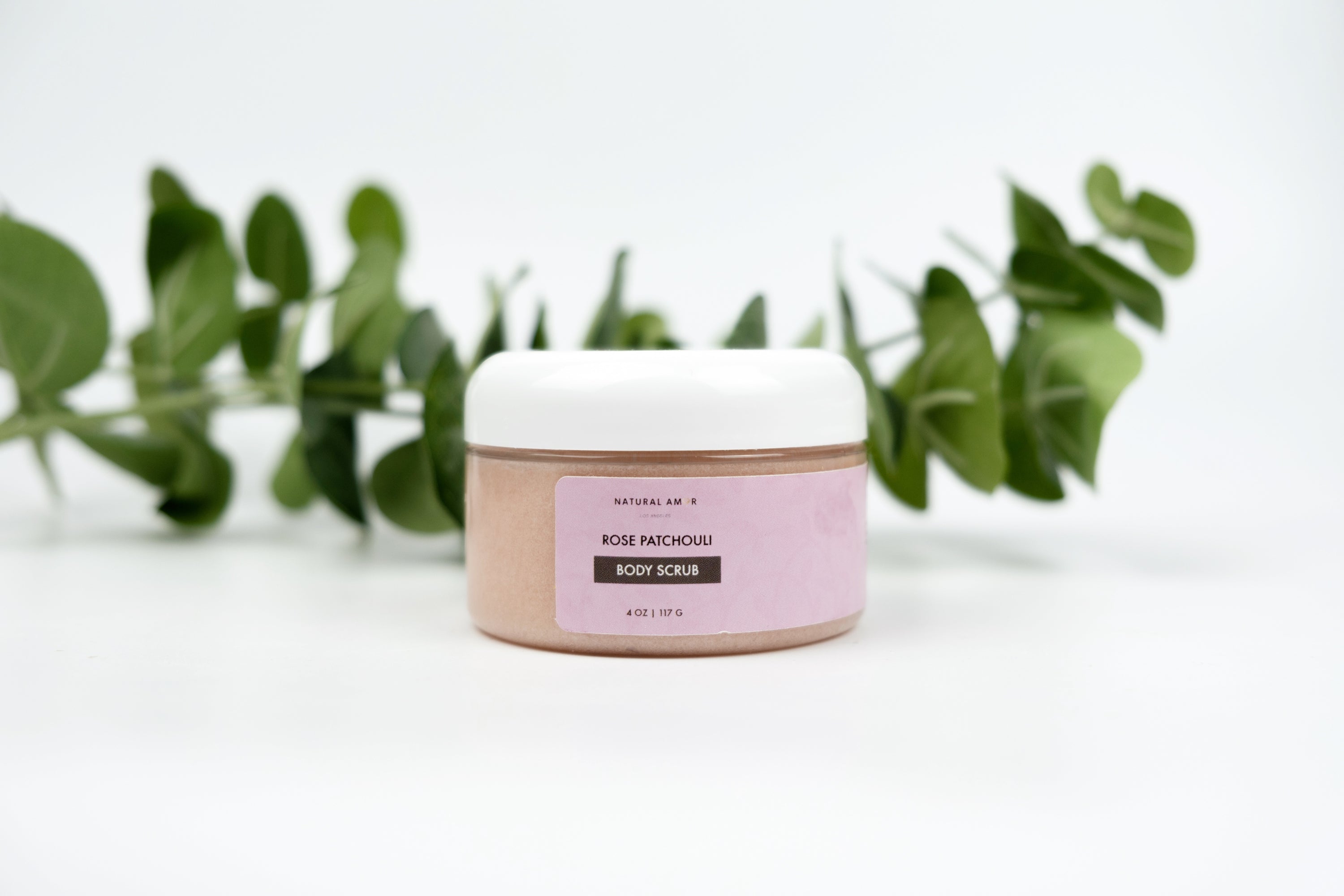 A jar of Rose Patchouli Body Scrub with a smooth texture, surrounded by rose petals and patchouli leaves, showcasing its natural ingredients.