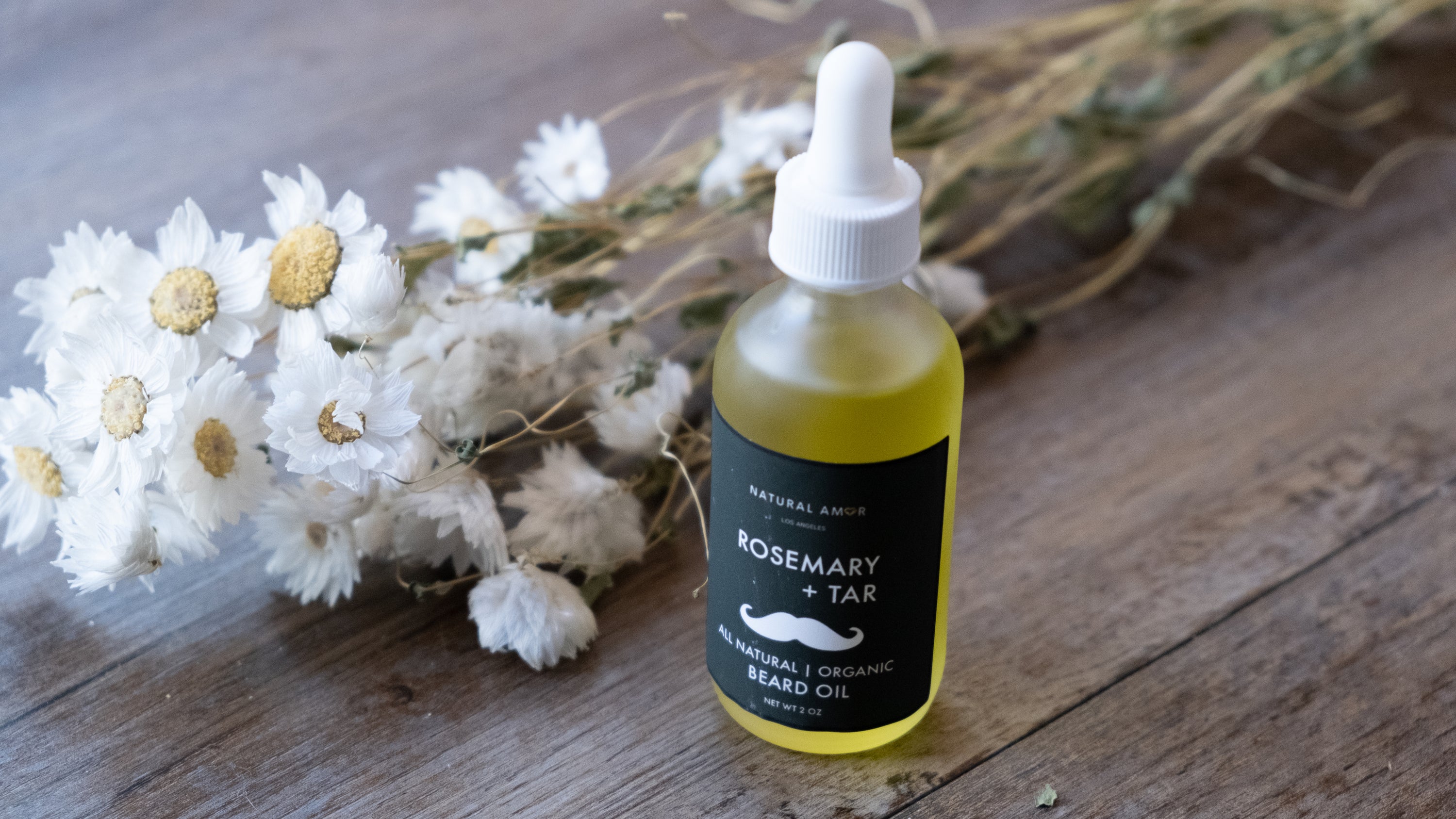 A frosted glass bottle of Rosemary+Tar Beard Oil with a dropper, showcasing its natural ingredients and elegant design.