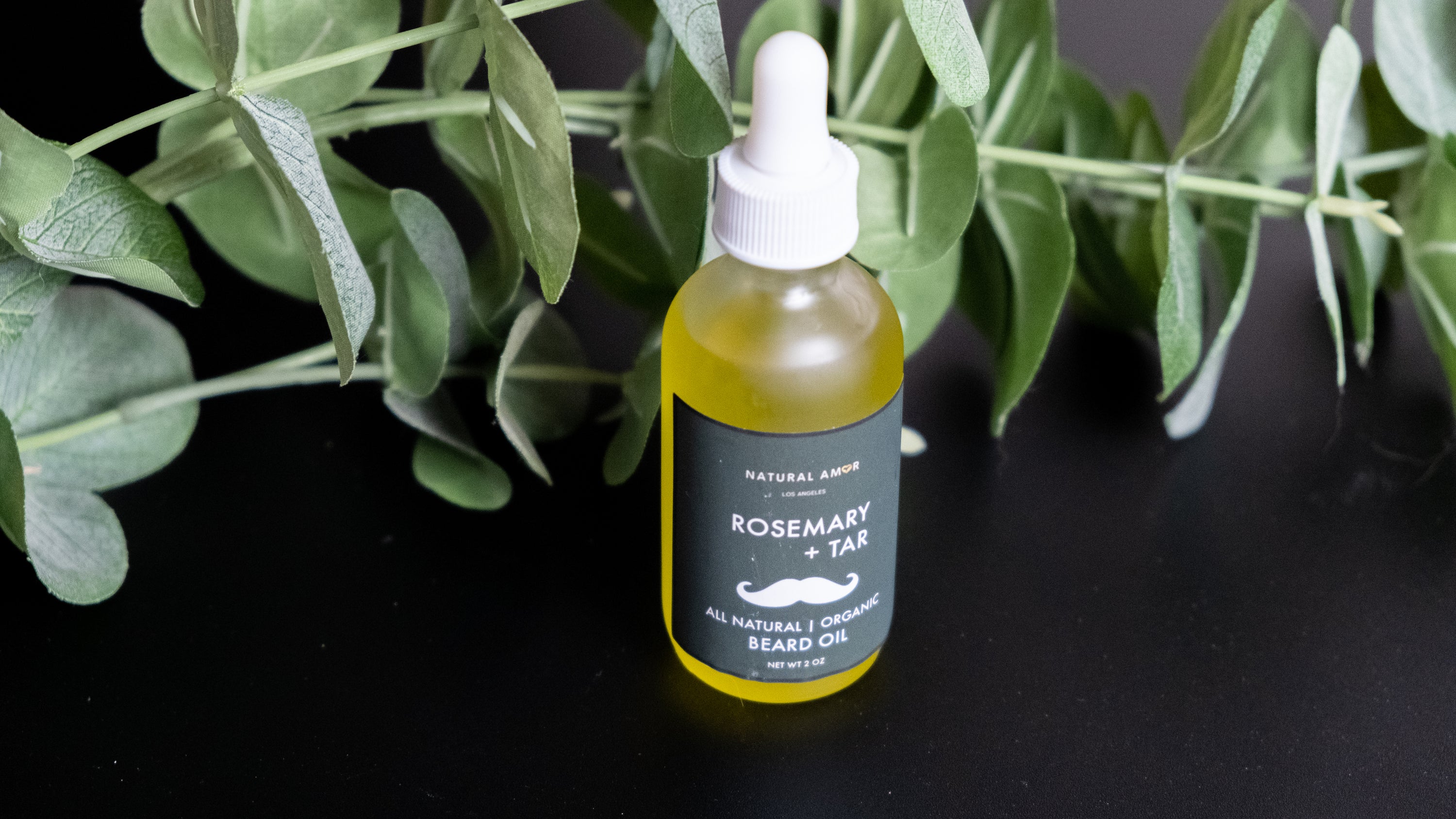 A frosted glass bottle of Rosemary+Tar Beard Oil with a dropper, showcasing its natural ingredients and elegant design.