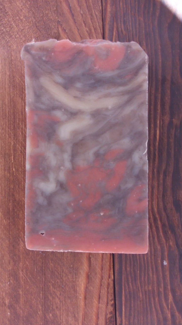 A bar of Sandalwood Soap showcasing its creamy texture and soft musk color, surrounded by natural ingredients.