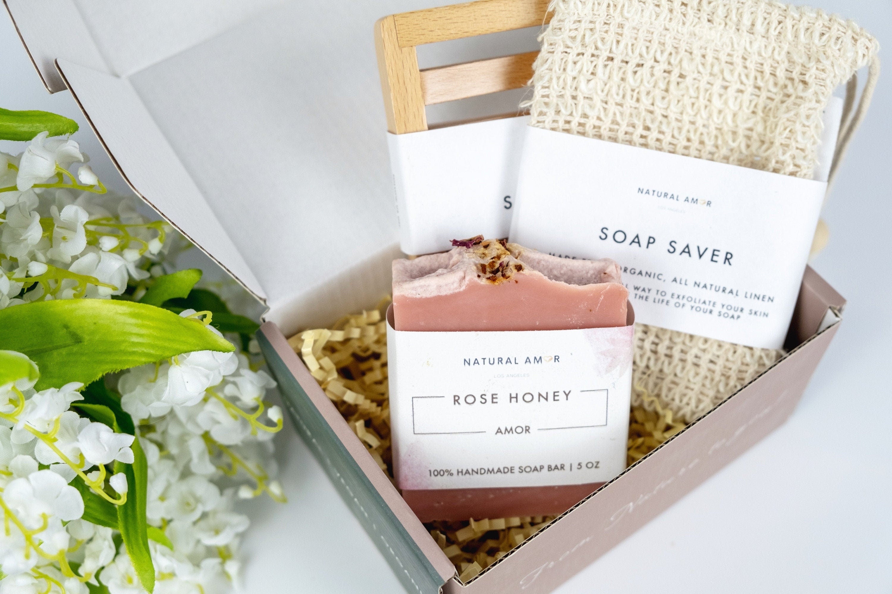 A beautifully arranged Simple Care Package Gift Box featuring a wooden soap dish, soap saver, and assorted handmade soaps in a printed gift box.