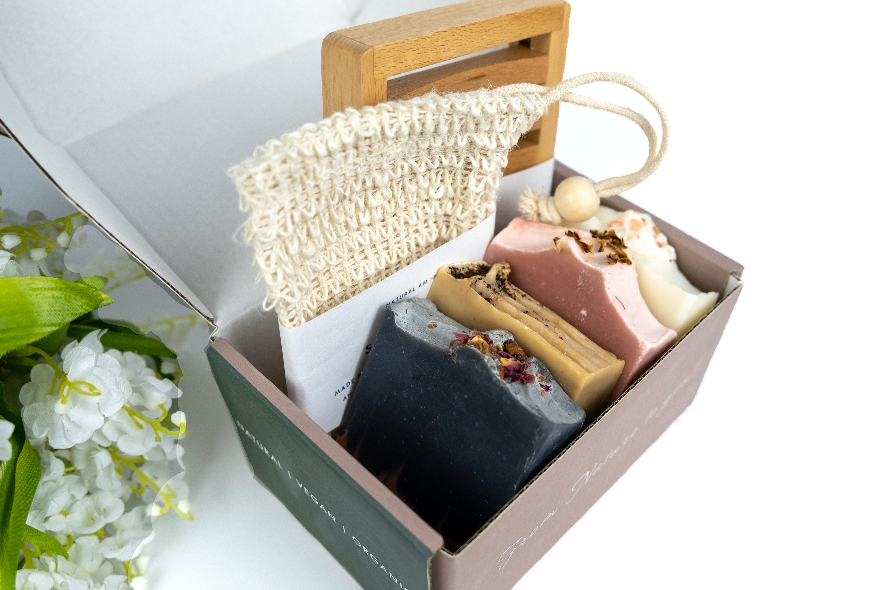 A beautifully arranged Simple Care Package Gift Box featuring a wooden soap dish, soap saver, and assorted handmade soaps in a printed gift box.