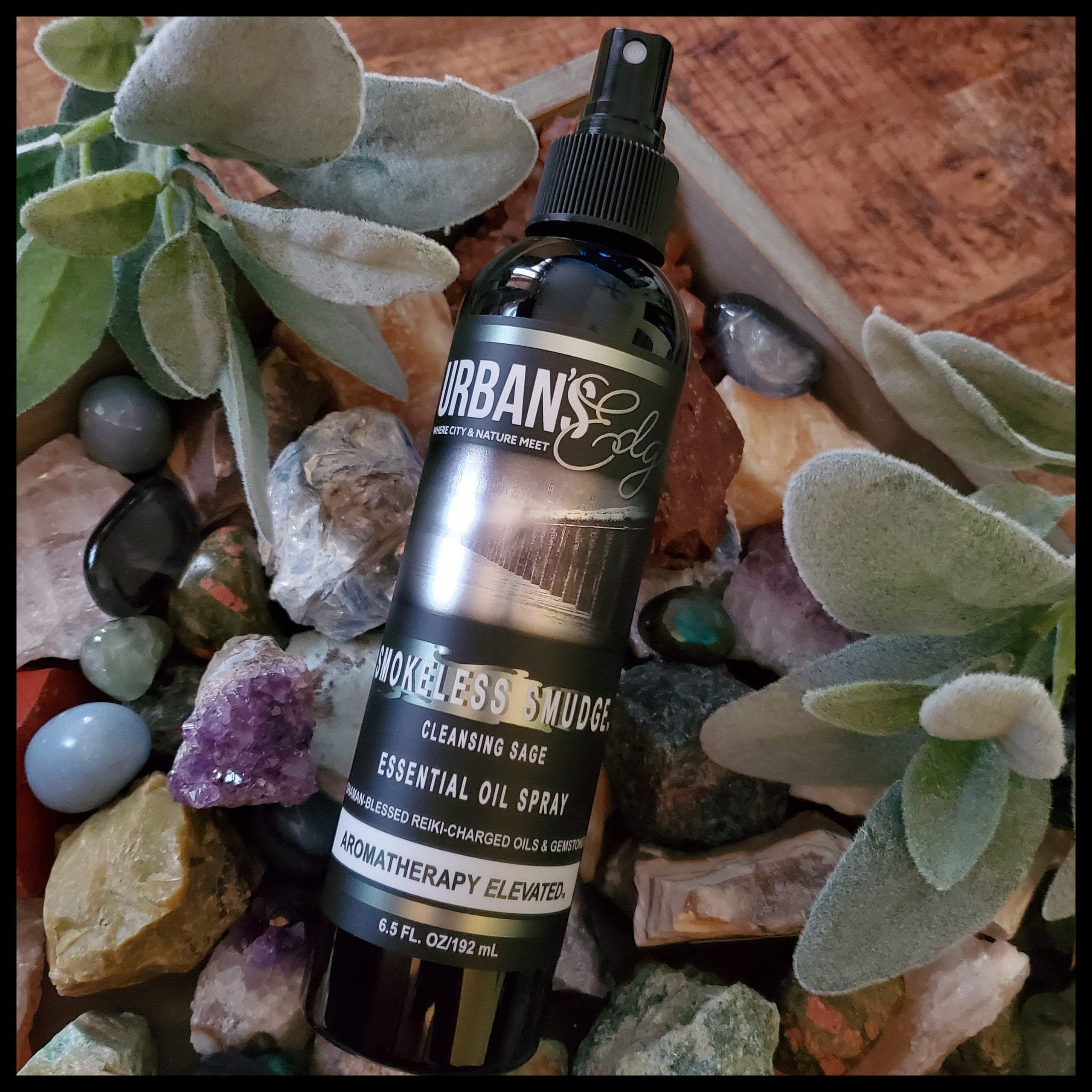 A bottle of Smokeless Smudge Essential Oil Spray with a misty spray effect, surrounded by gemstones and natural elements.