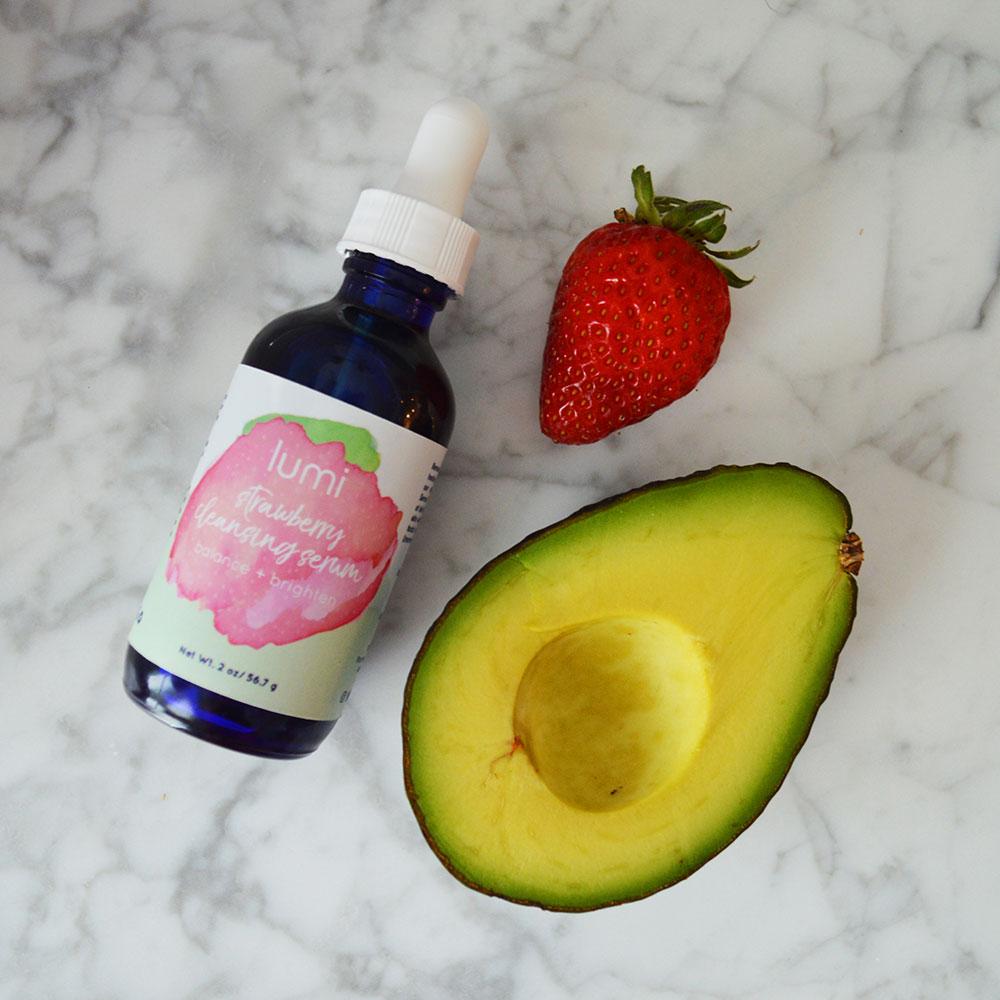 A bottle of Strawberry Cleansing Serum with a vibrant label, surrounded by fresh strawberries and natural ingredients.