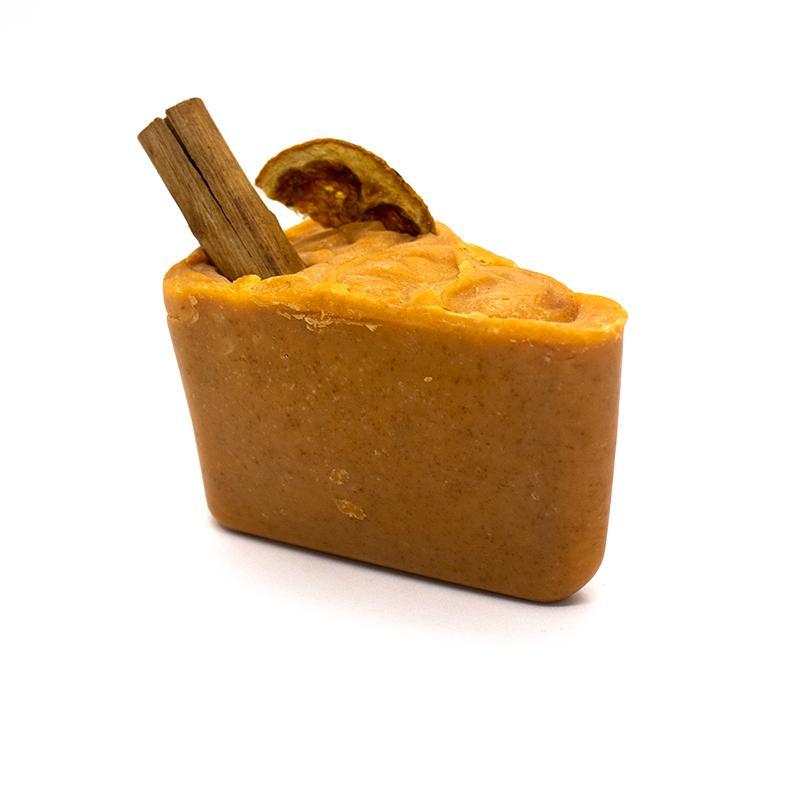 A beautifully crafted 'Sugar and Spice' soap featuring dried orange and a cinnamon stick, showcasing its vibrant orange color.