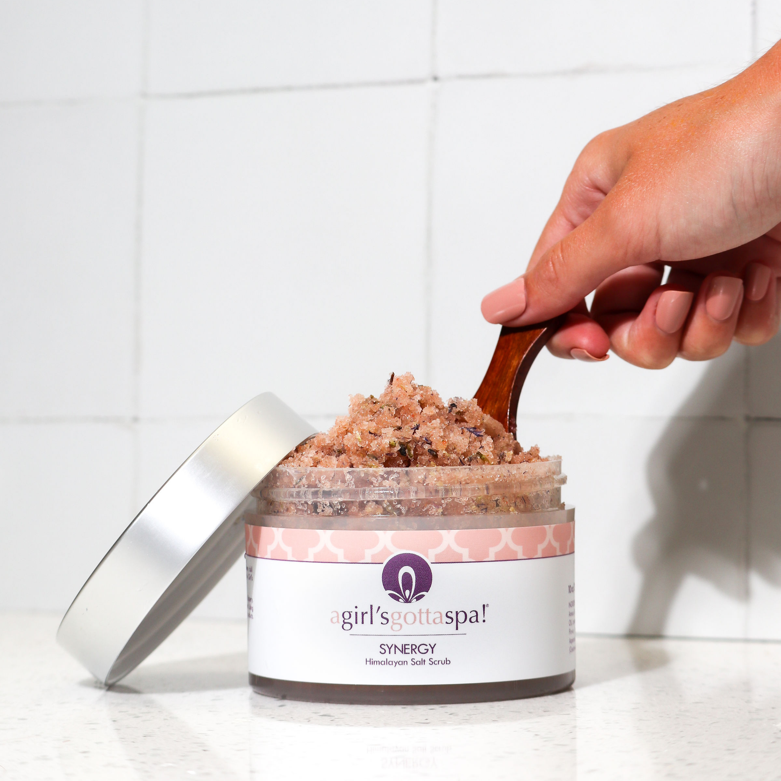 A jar of Synergy Himalayan Salt Body Scrub with a wooden spoon, showcasing its natural pink salt texture and aromatic ingredients.