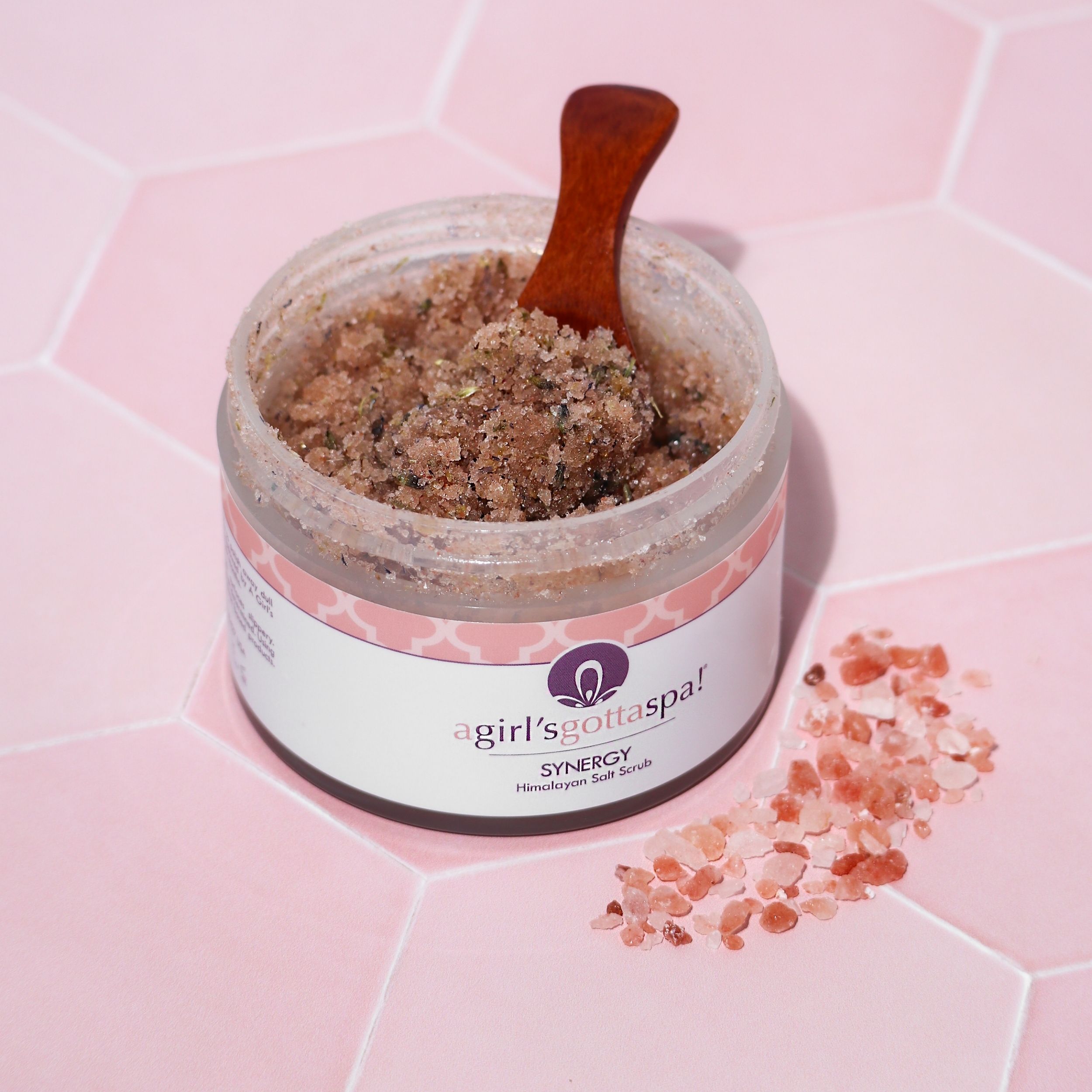 A jar of Synergy Himalayan Salt Body Scrub with a wooden spoon, showcasing its natural pink salt texture and aromatic ingredients.