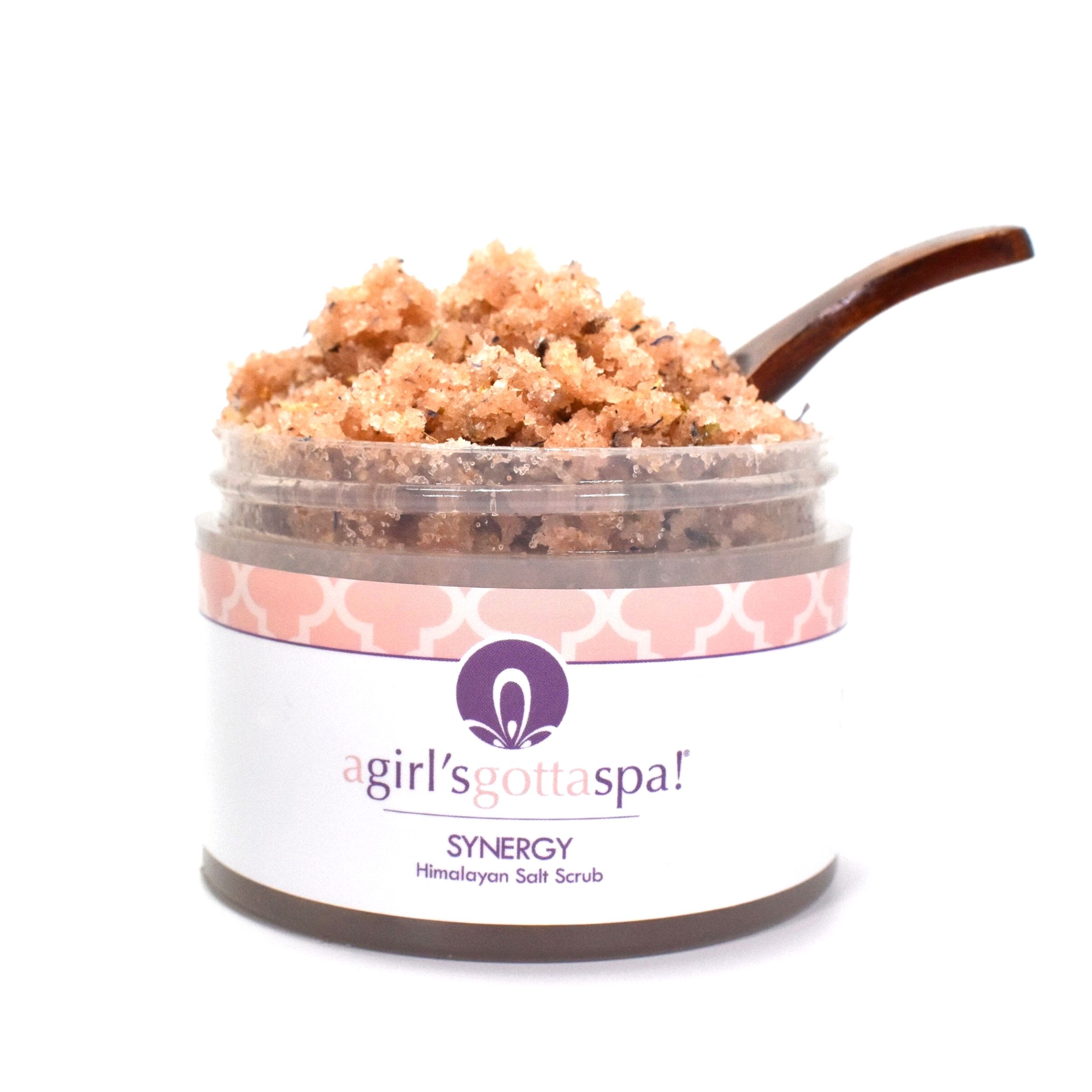 A jar of Synergy Himalayan Salt Body Scrub with a wooden spoon, showcasing its natural pink salt texture and aromatic ingredients.