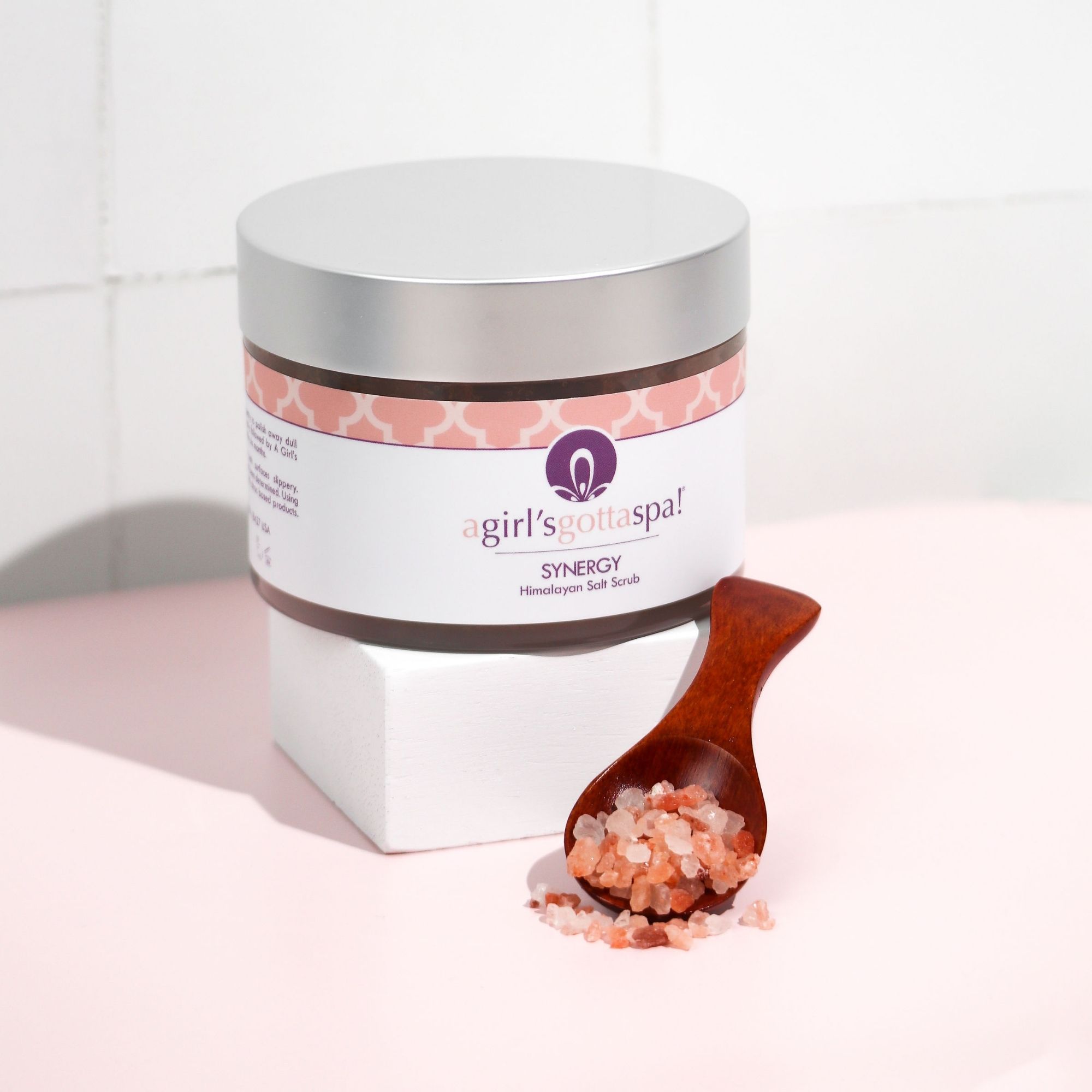 A jar of Synergy Himalayan Salt Body Scrub with a wooden spoon, showcasing its natural pink salt texture and aromatic ingredients.