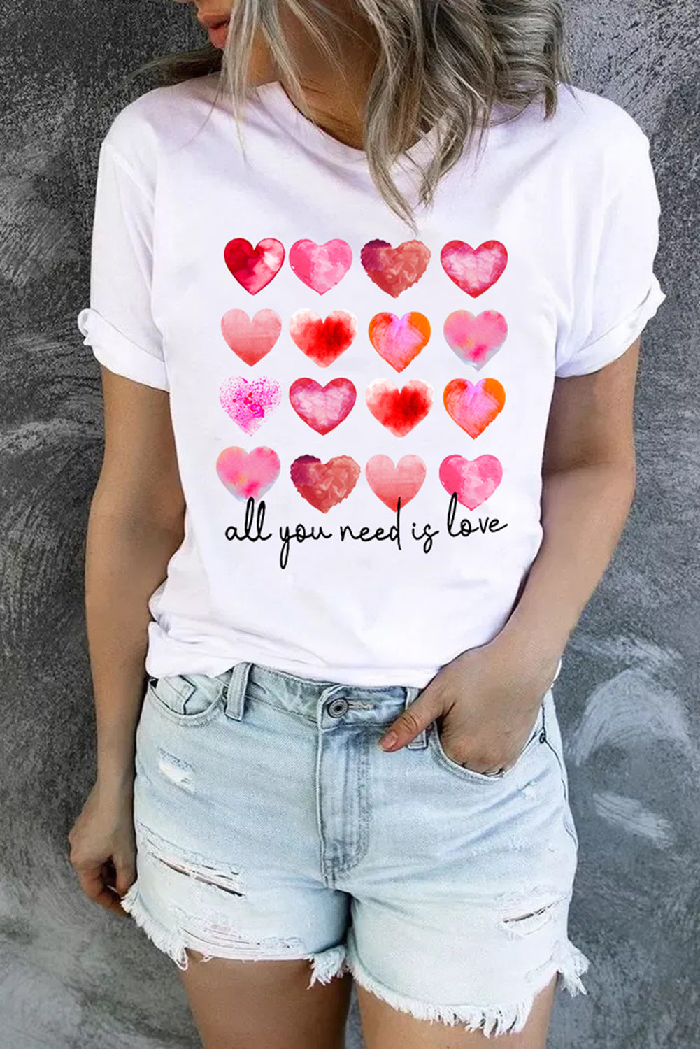 White t-shirt featuring a colorful hearts print with the text 'All You Need Is Love', perfect for casual wear.