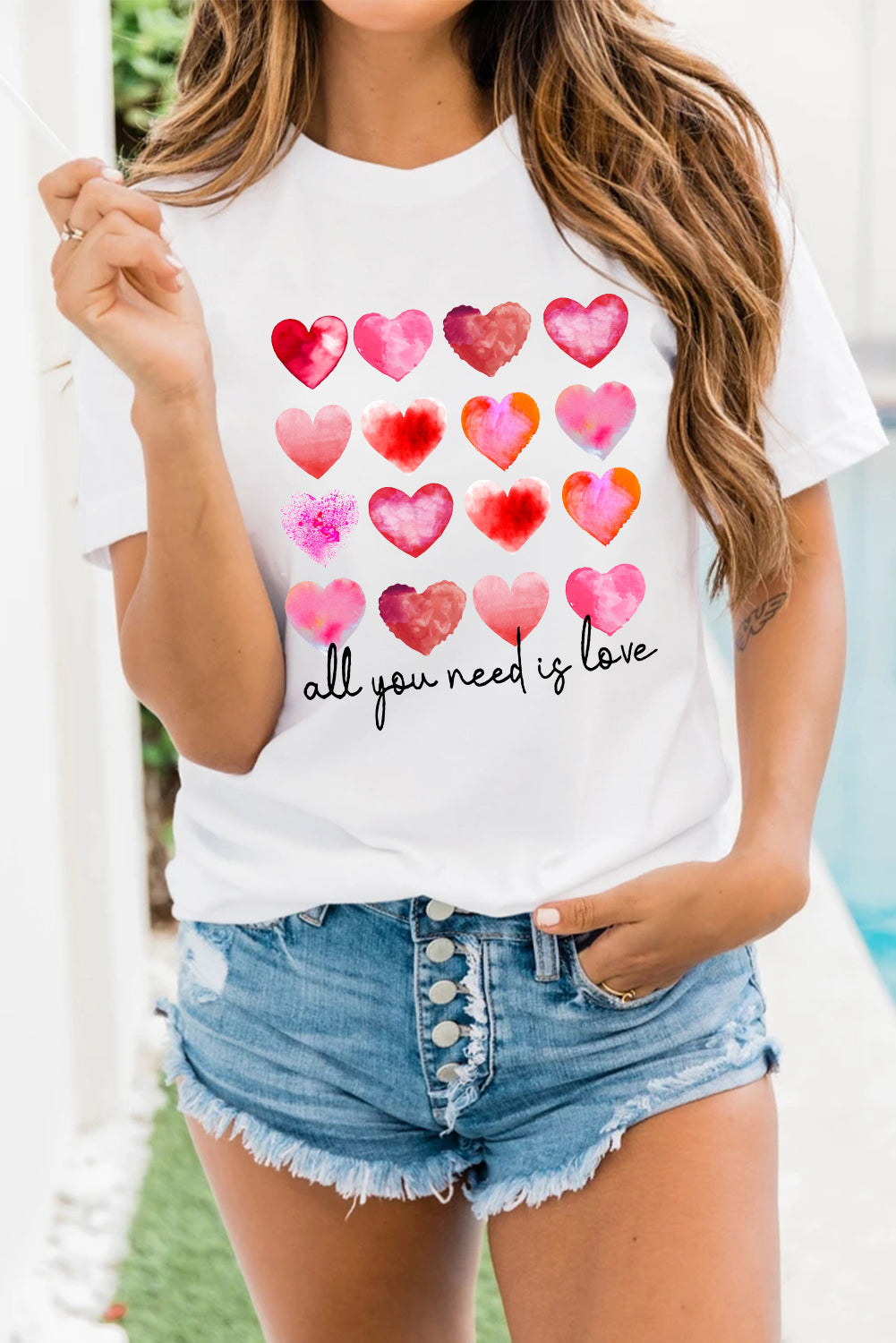 White t-shirt featuring a colorful hearts print with the text 'All You Need Is Love', perfect for casual wear.