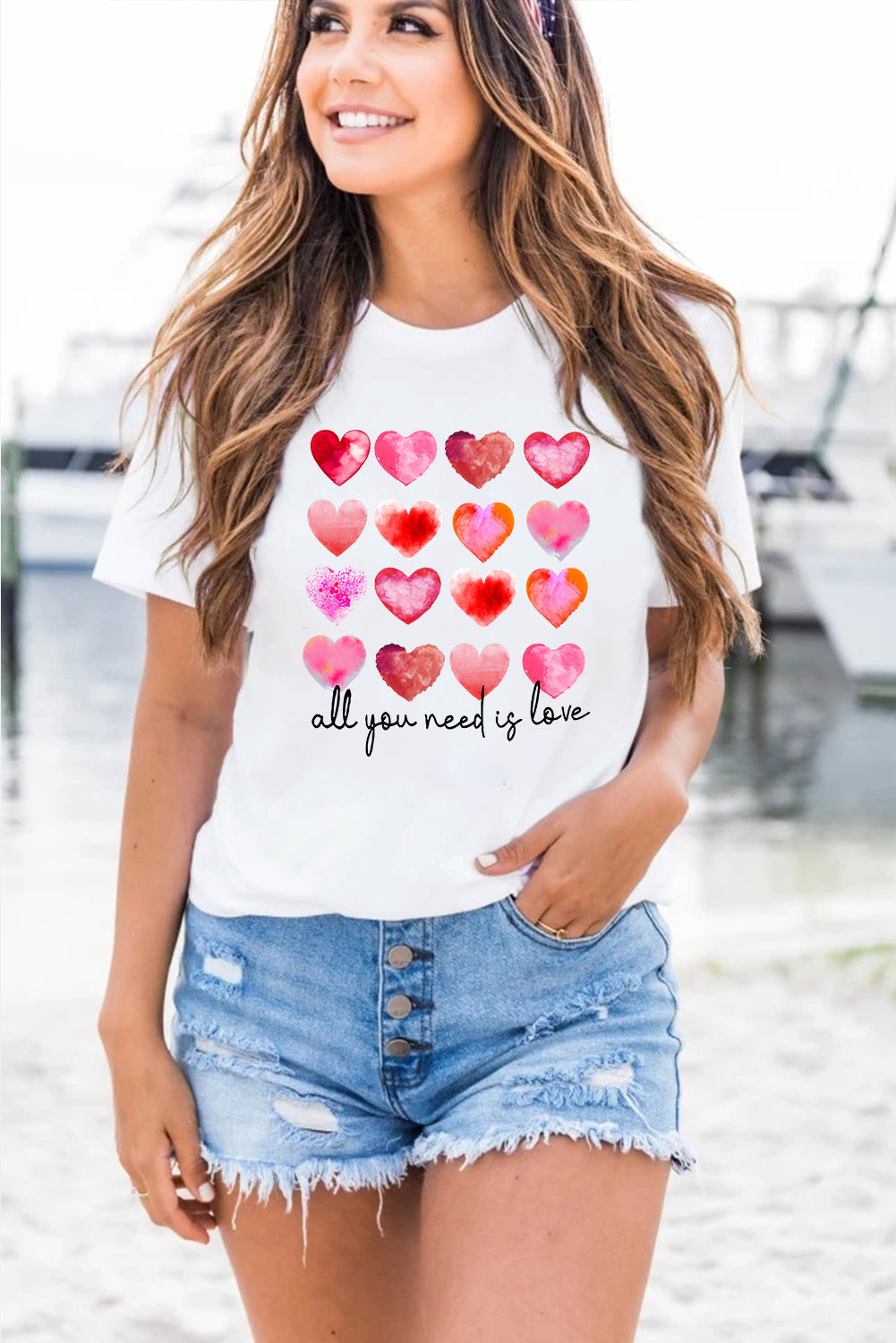 White t-shirt featuring a colorful hearts print with the text 'All You Need Is Love', perfect for casual wear.