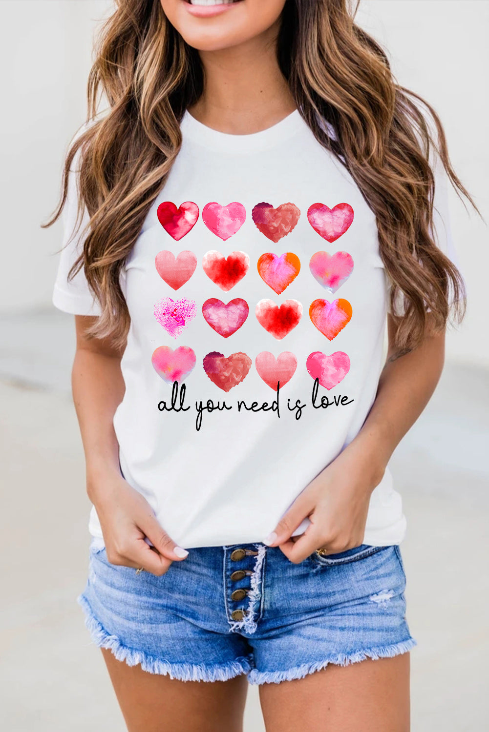 White t-shirt featuring a colorful hearts print with the text 'All You Need Is Love', perfect for casual wear.