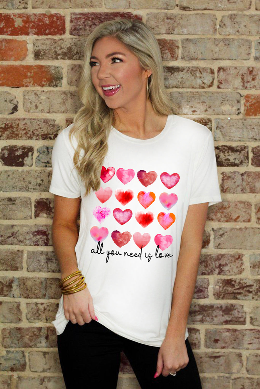 White t-shirt featuring a colorful hearts print with the text 'All You Need Is Love', perfect for casual wear.