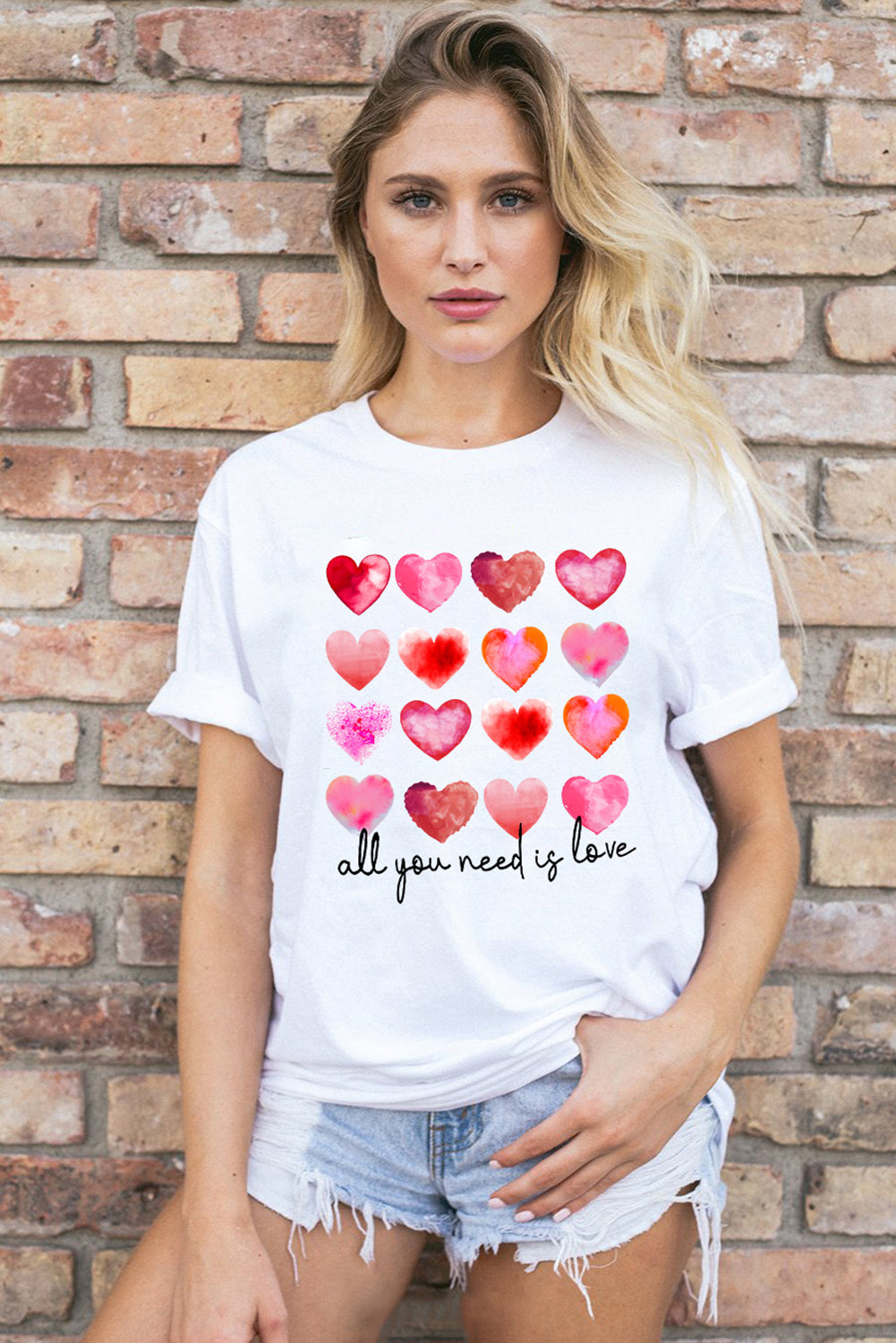 White t-shirt featuring a colorful hearts print with the text 'All You Need Is Love', perfect for casual wear.