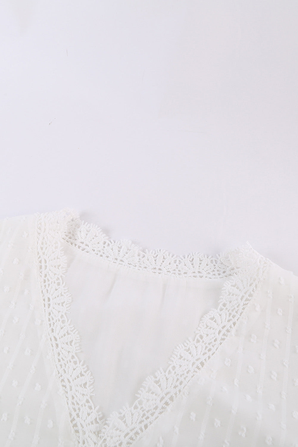 A stylish white blouse featuring a v-neck design, swiss dot pattern, and lace trim on the neckline and sleeves, perfect for casual or formal wear.