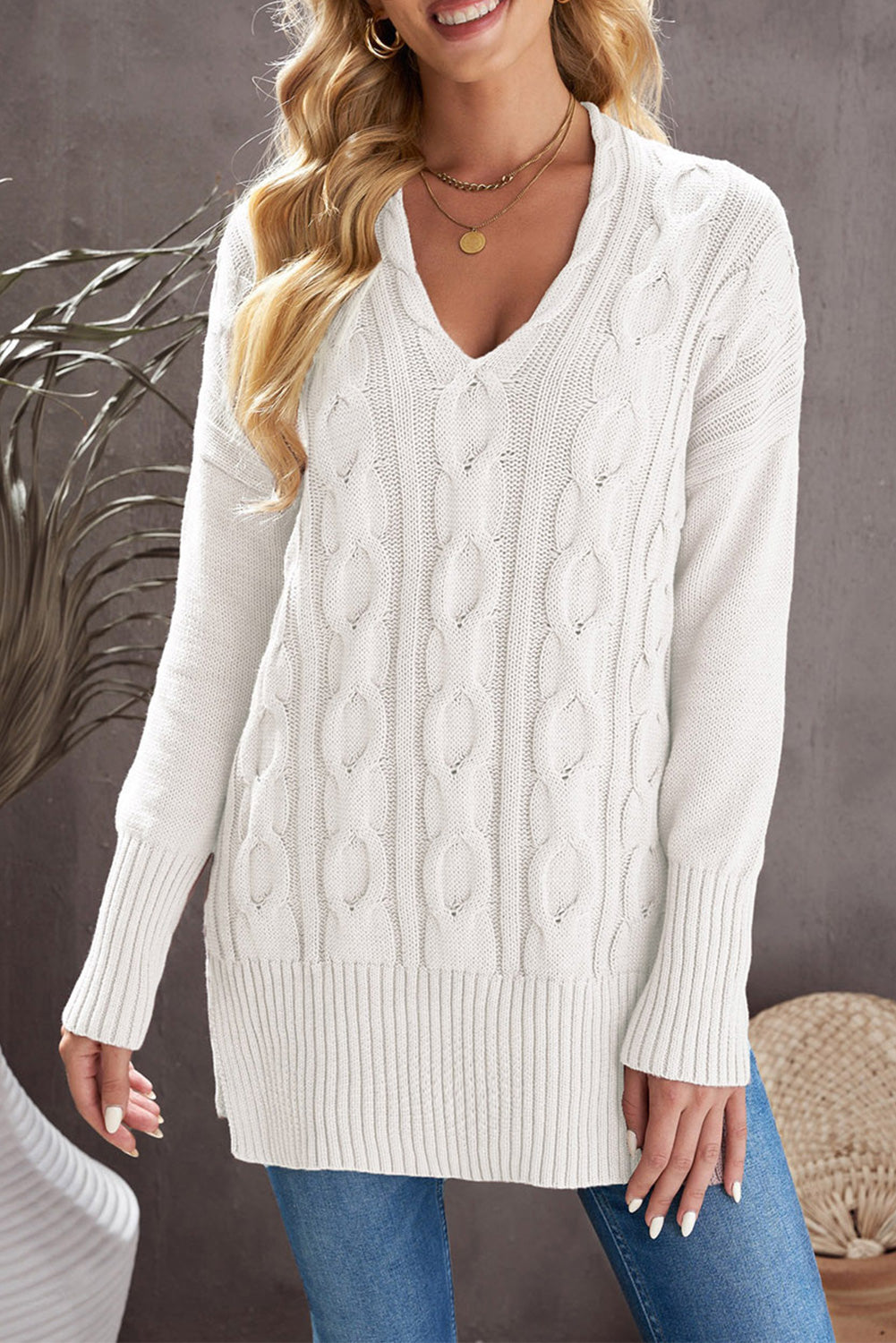 A stylish white oversized knit sweater with a deep v-neck and side slits, perfect for cozy wear.