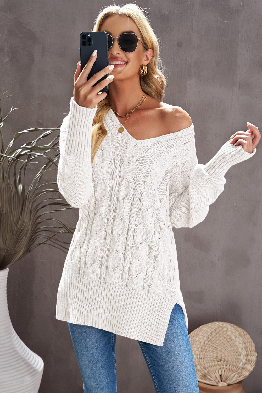 A stylish white oversized knit sweater with a deep v-neck and side slits, perfect for cozy wear.