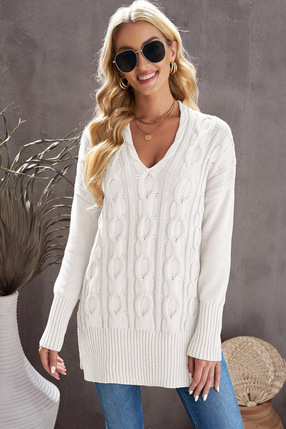 A stylish white oversized knit sweater with a deep v-neck and side slits, perfect for cozy wear.