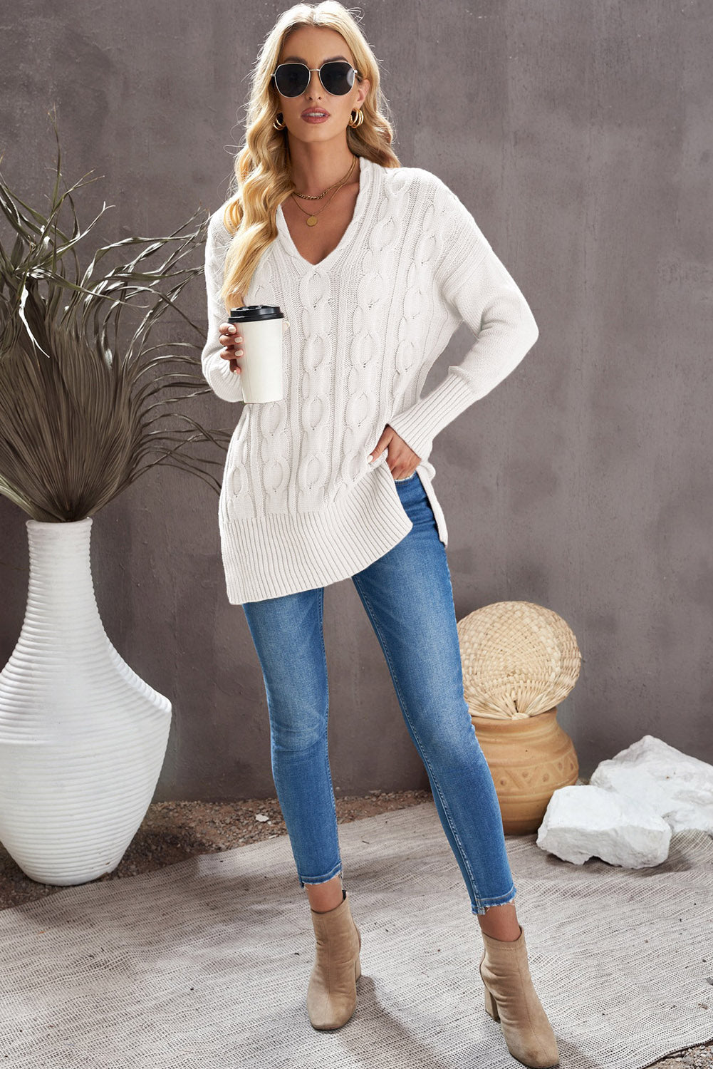 A stylish white oversized knit sweater with a deep v-neck and side slits, perfect for cozy wear.