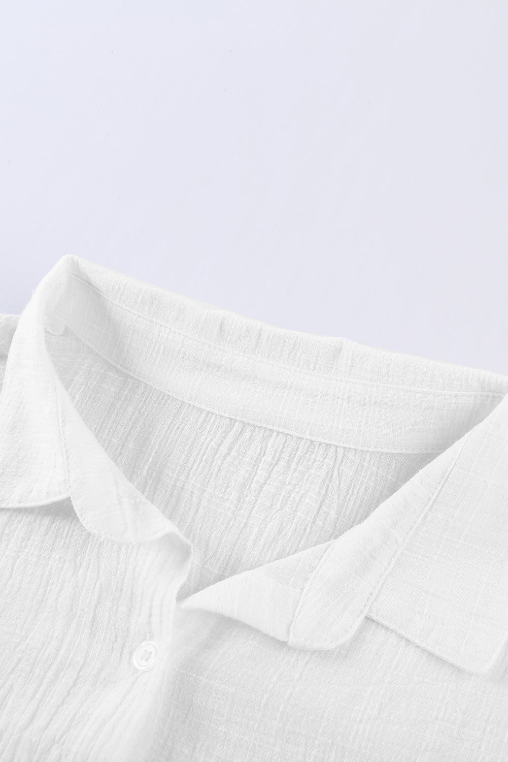 A stylish white textured solid color basic shirt featuring a button closure and collar, showcasing its elegant design and lightweight fabric.