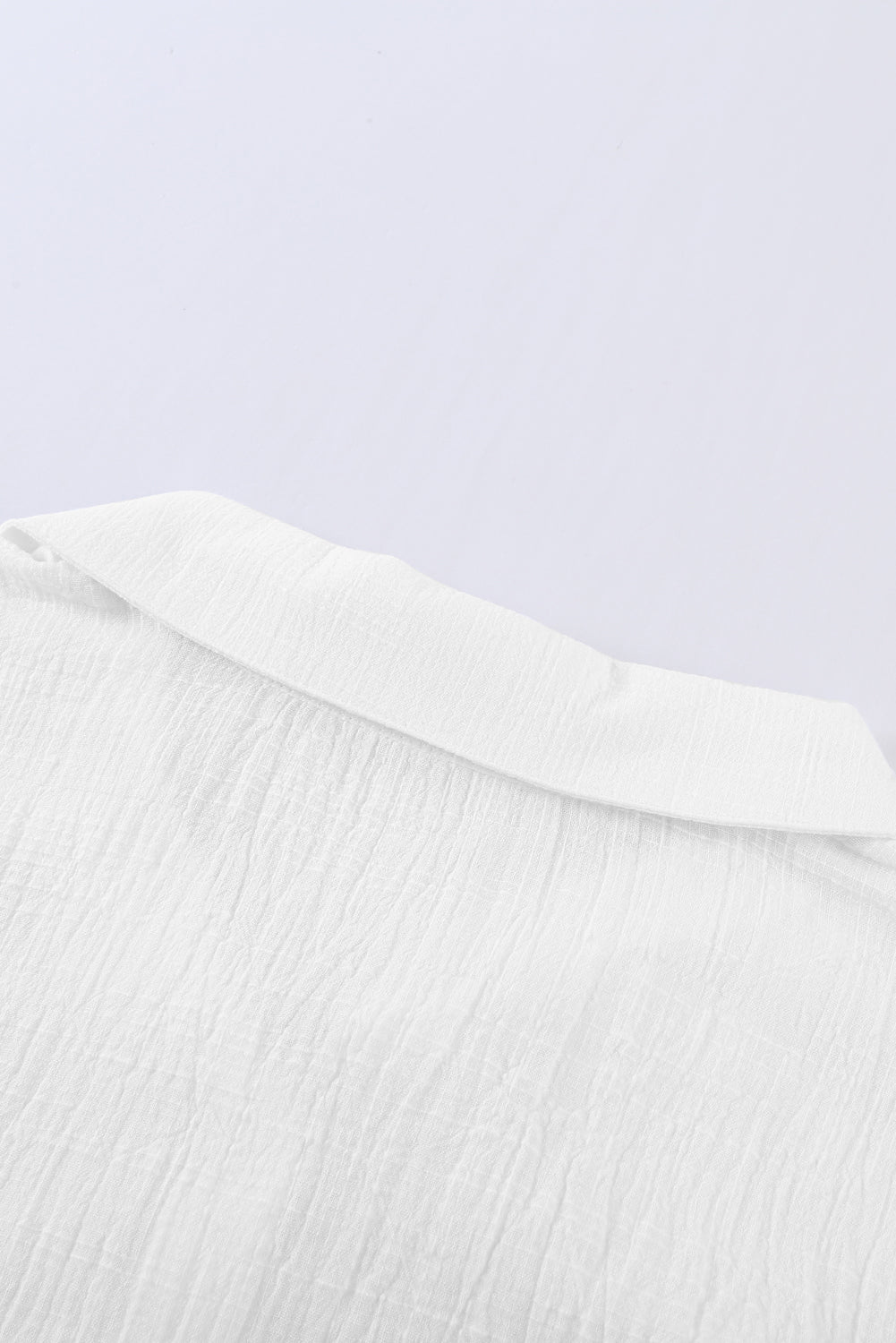 A stylish white textured solid color basic shirt featuring a button closure and collar, showcasing its elegant design and lightweight fabric.