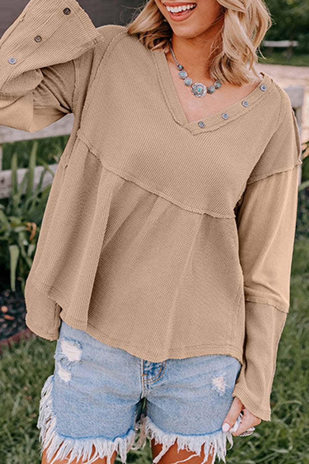 A stylish white waffle knit top featuring button details at the neckline and exposed seam accents, showcasing a relaxed fit and wavy raw hemline.