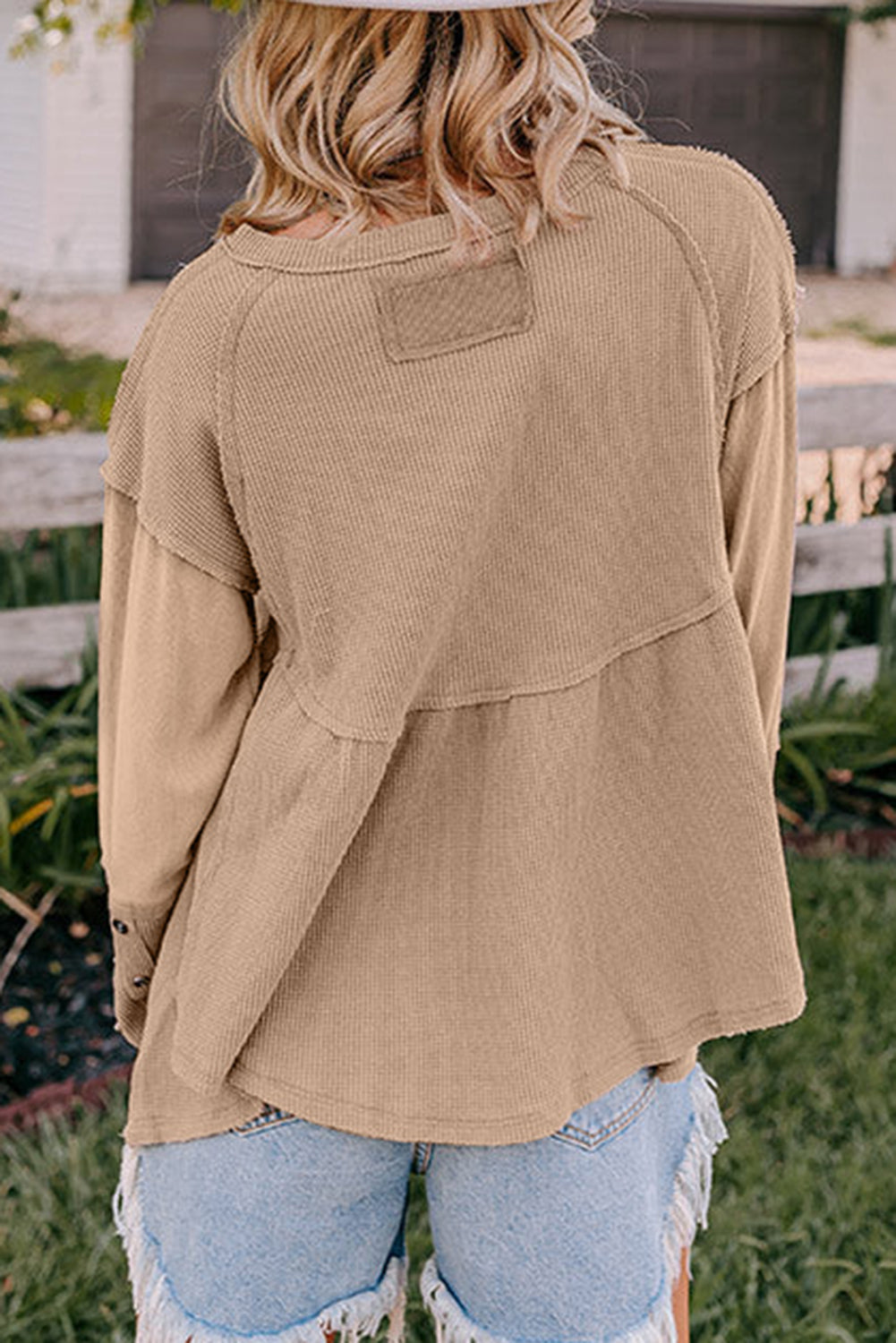 A stylish white waffle knit top featuring button details at the neckline and exposed seam accents, showcasing a relaxed fit and wavy raw hemline.