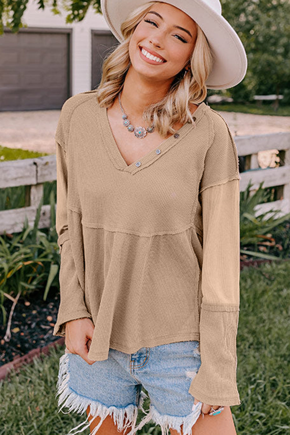 A stylish white waffle knit top featuring button details at the neckline and exposed seam accents, showcasing a relaxed fit and wavy raw hemline.