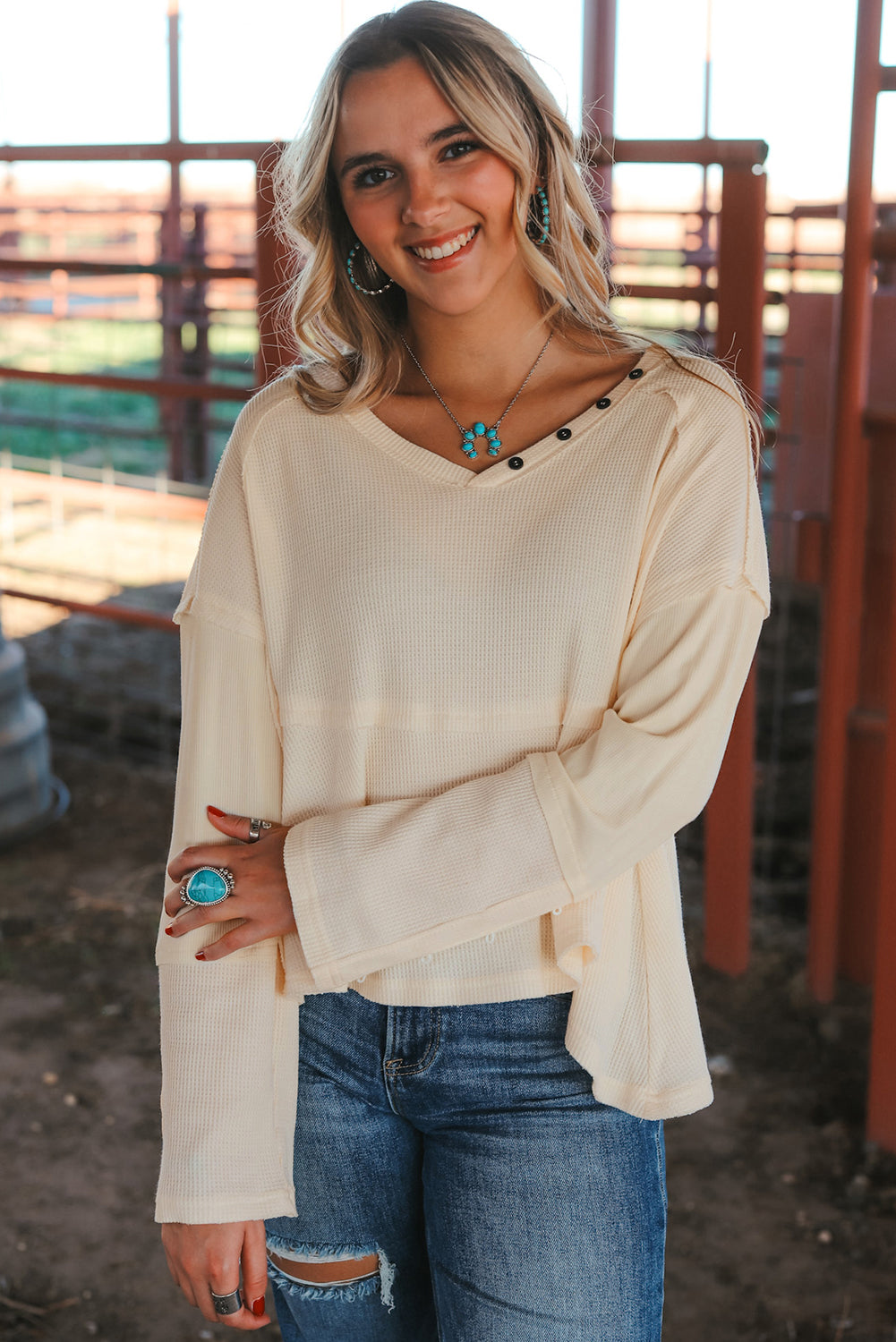 A stylish white waffle knit top featuring button details at the neckline and exposed seam accents, showcasing a relaxed fit and wavy raw hemline.