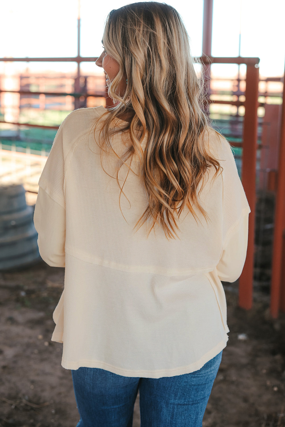 A stylish white waffle knit top featuring button details at the neckline and exposed seam accents, showcasing a relaxed fit and wavy raw hemline.