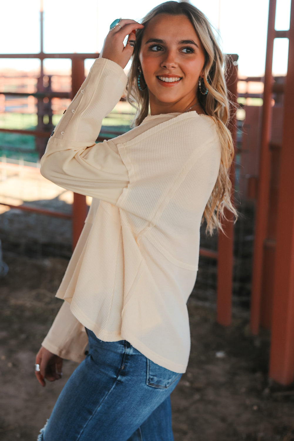 A stylish white waffle knit top featuring button details at the neckline and exposed seam accents, showcasing a relaxed fit and wavy raw hemline.