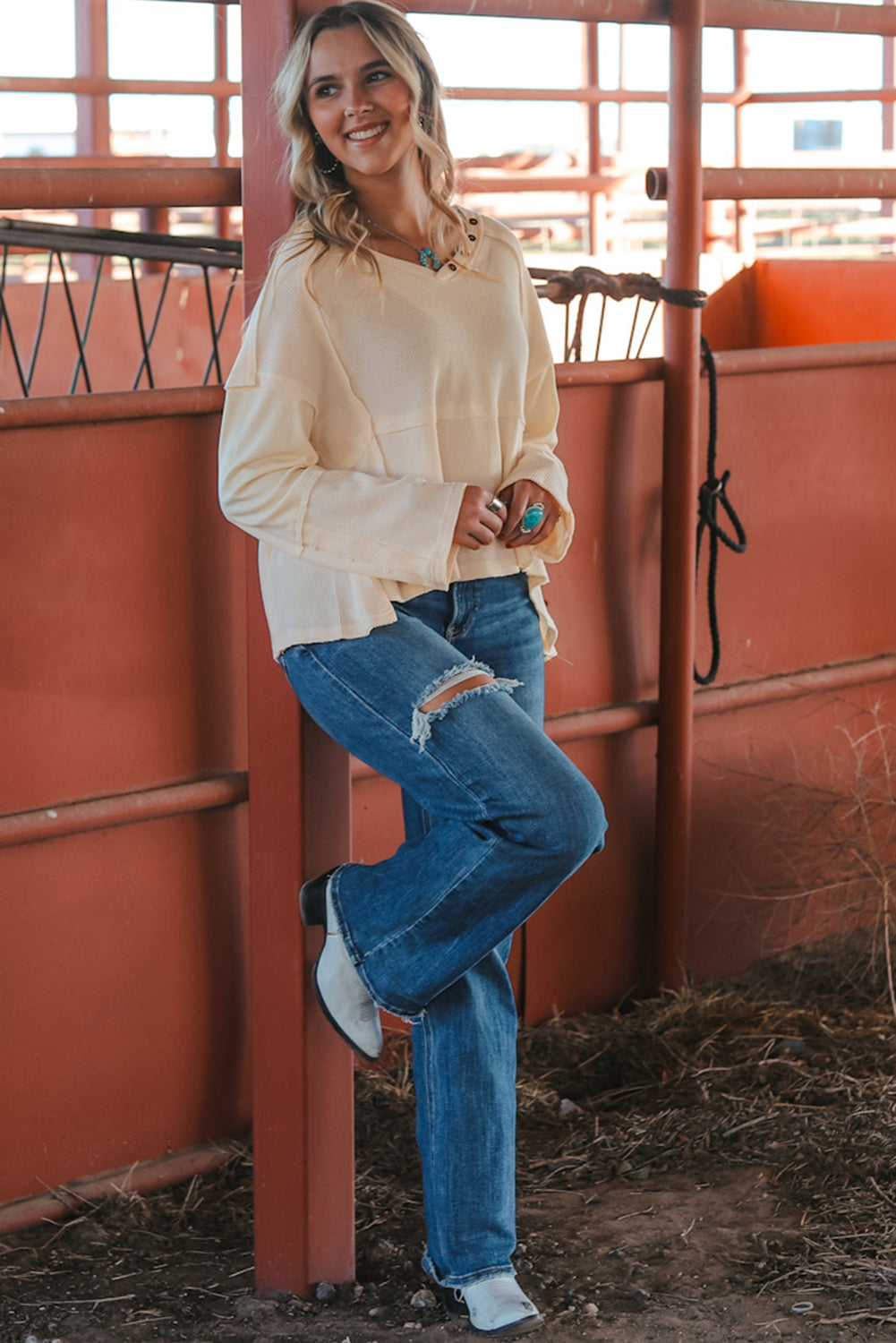 A stylish white waffle knit top featuring button details at the neckline and exposed seam accents, showcasing a relaxed fit and wavy raw hemline.