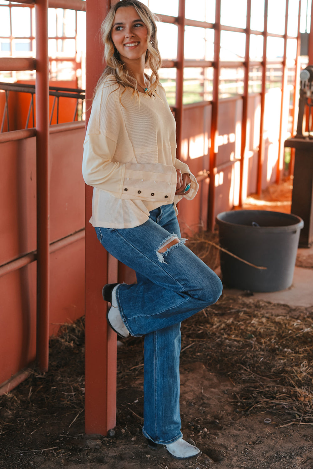 A stylish white waffle knit top featuring button details at the neckline and exposed seam accents, showcasing a relaxed fit and wavy raw hemline.