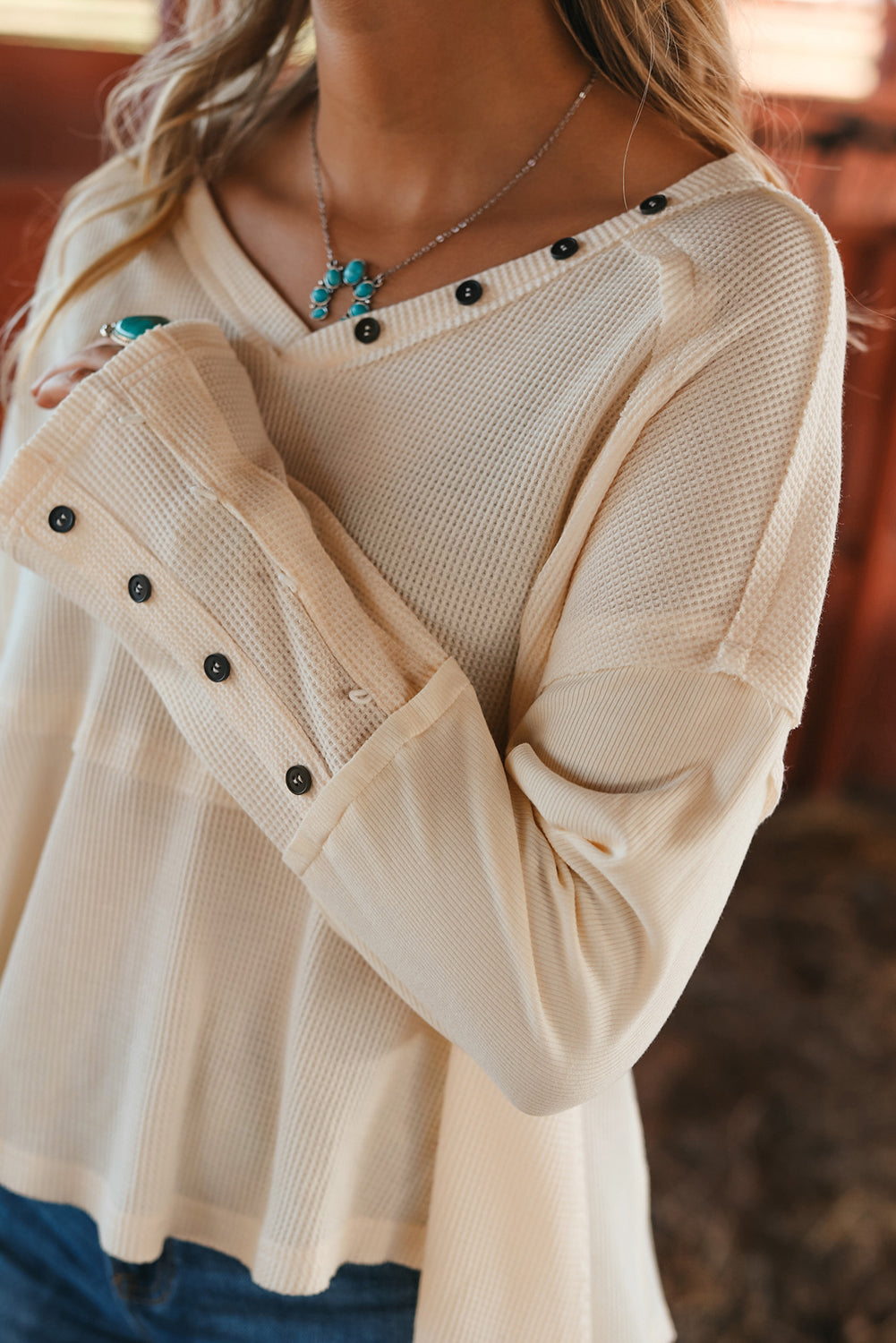 A stylish white waffle knit top featuring button details at the neckline and exposed seam accents, showcasing a relaxed fit and wavy raw hemline.