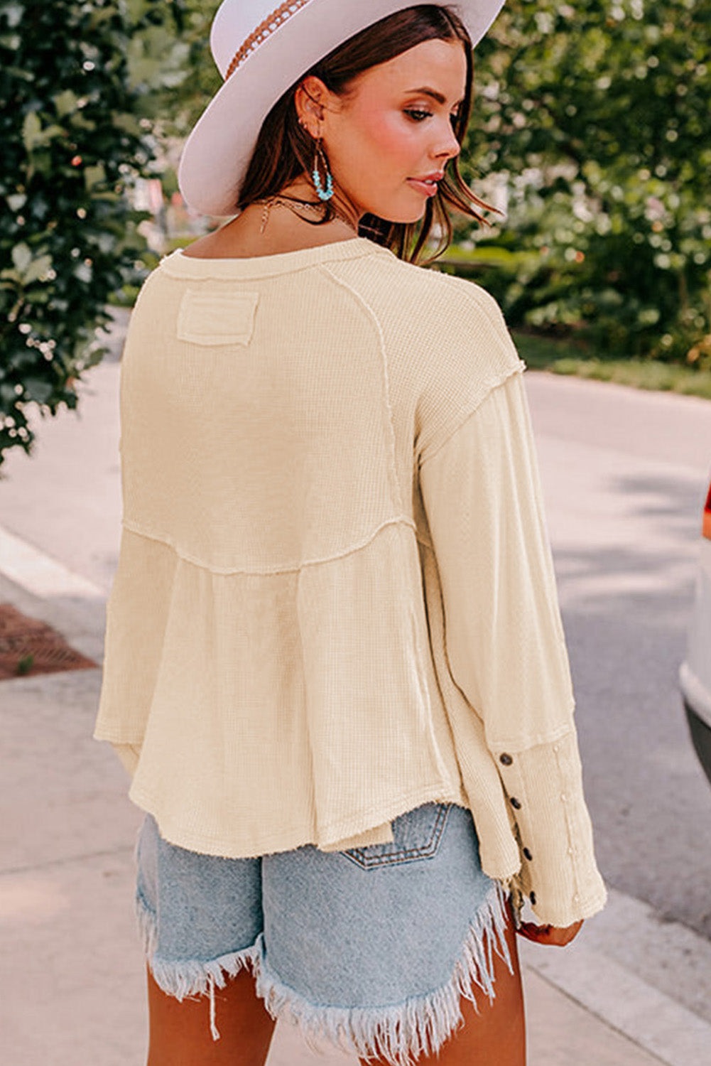 A stylish white waffle knit top featuring button details at the neckline and exposed seam accents, showcasing a relaxed fit and wavy raw hemline.