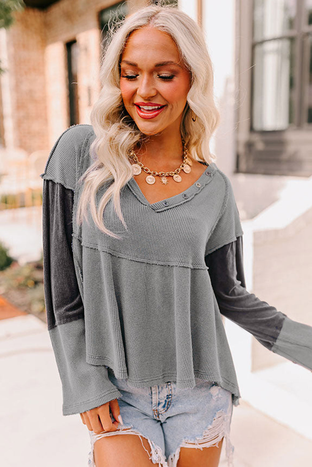 A stylish white waffle knit top featuring button details at the neckline and exposed seam accents, showcasing a relaxed fit and wavy raw hemline.