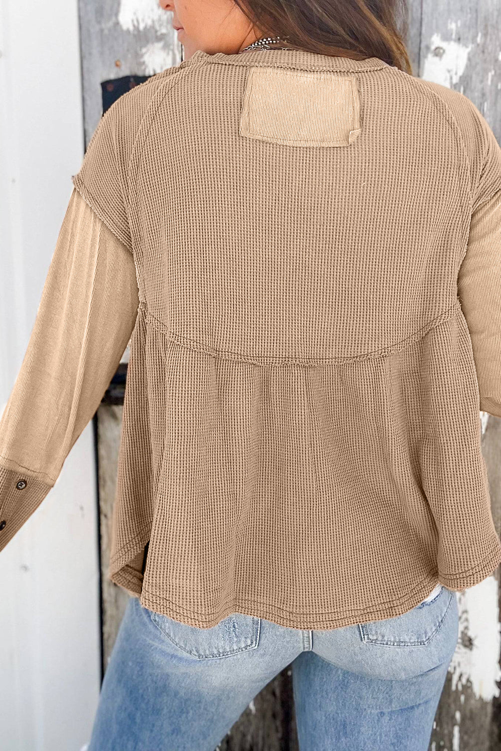 A stylish white waffle knit top featuring button details at the neckline and exposed seam accents, showcasing a relaxed fit and wavy raw hemline.