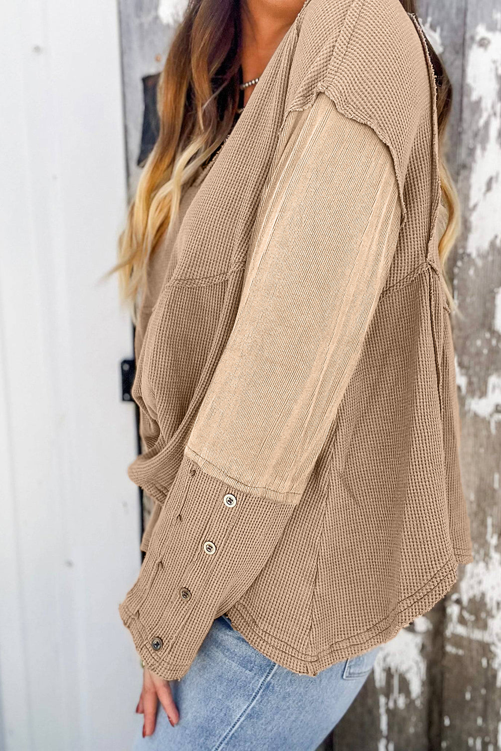 A stylish white waffle knit top featuring button details at the neckline and exposed seam accents, showcasing a relaxed fit and wavy raw hemline.